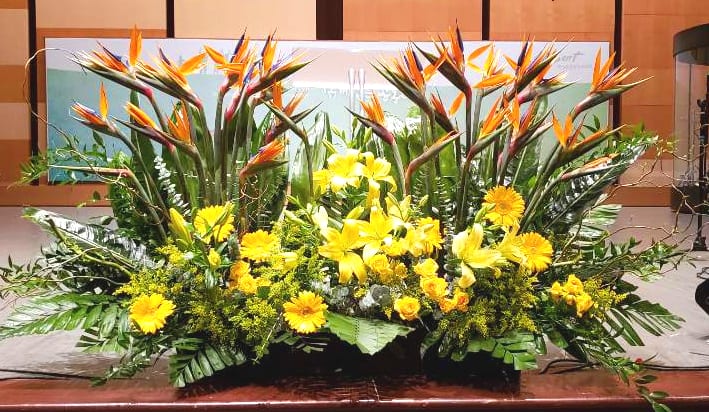 Large tropical arrangement with orange birds of paradise and yellow flowers in a low front-facing display
