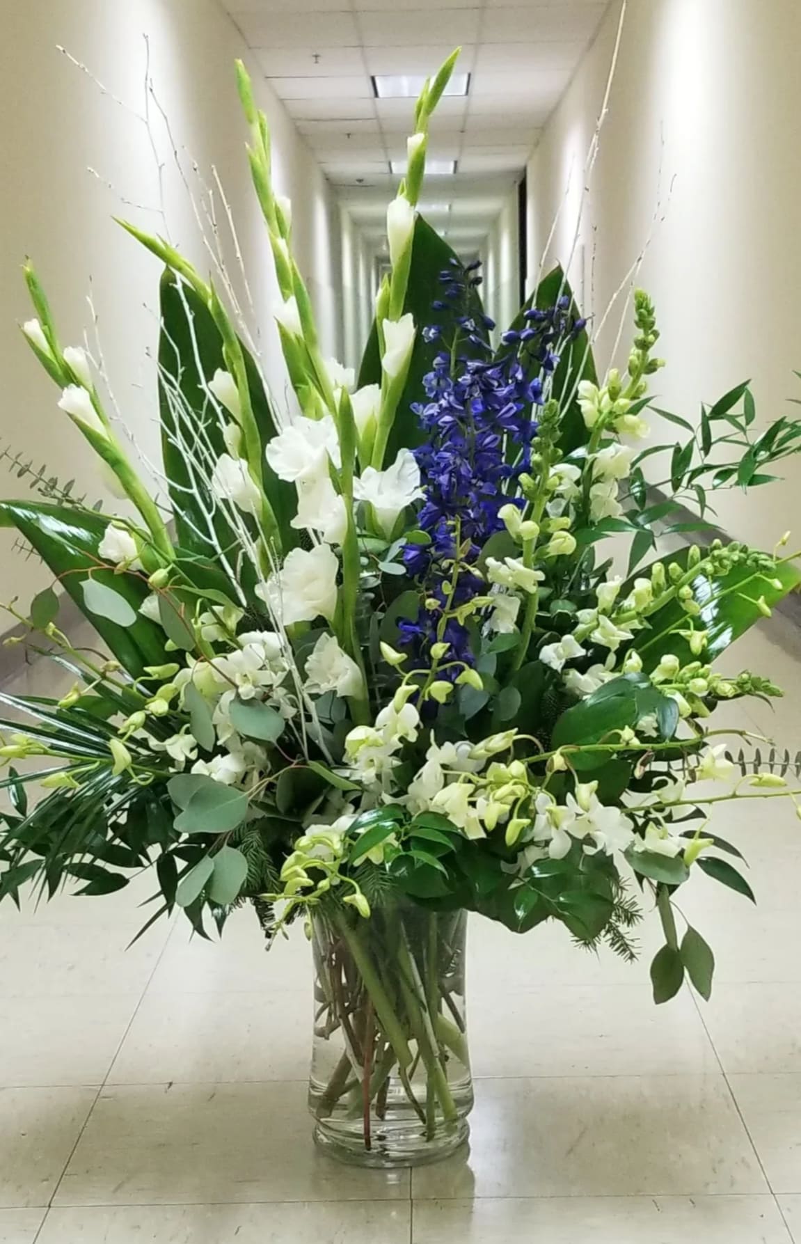 Tall floral arrangement in a clear glass vase with white and blue blooms