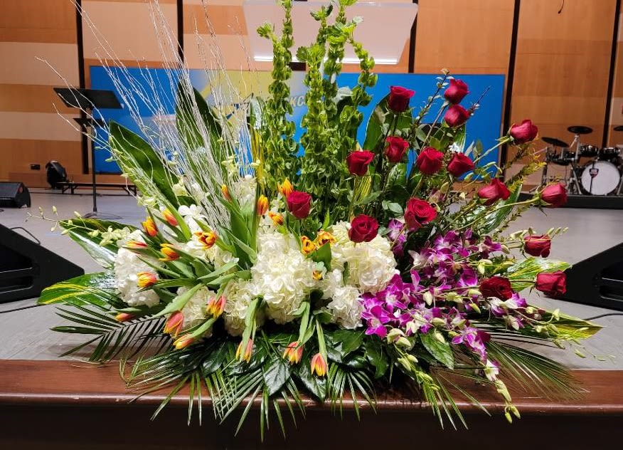 Large mixed floral spray with red roses, white hydrangeas, yellow-red tulips, and purple orchids.