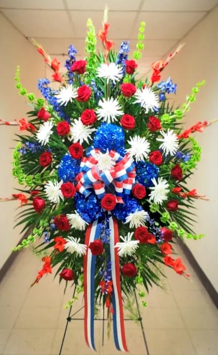 Patriotic standing spray of red roses, white mums, and blue accents with striped bow on an easel