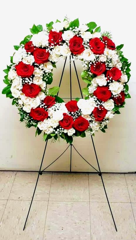 Standing wreath of red and white roses with white filler flowers on a metal easel.