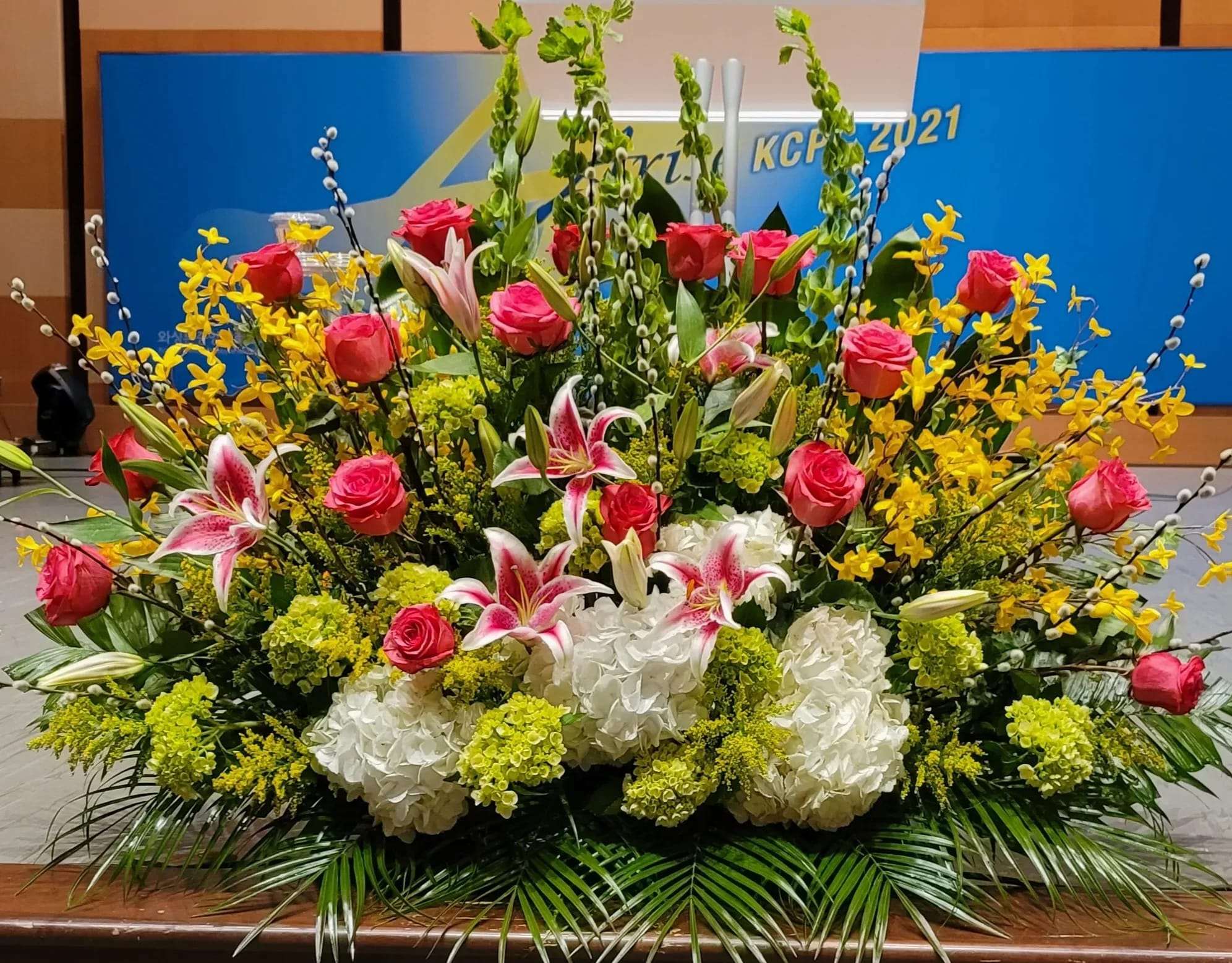 Large stage floral arrangement with pink roses, stargazer lilies, white hydrangeas and yellow flowers