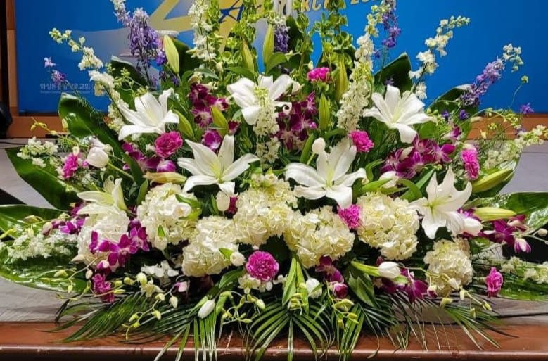 Large white and purple altar-style flower arrangement with lilies, hydrangeas, and orchids