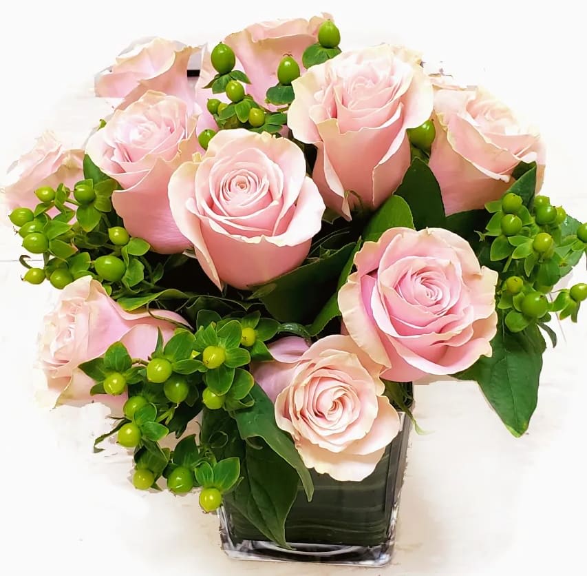 Pink roses arranged in a clear square vase with green berries