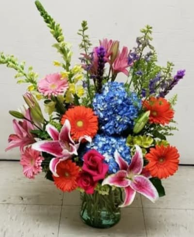Colorful mixed bouquet in a glass vase with lilies, gerberas, roses, and hydrangeas