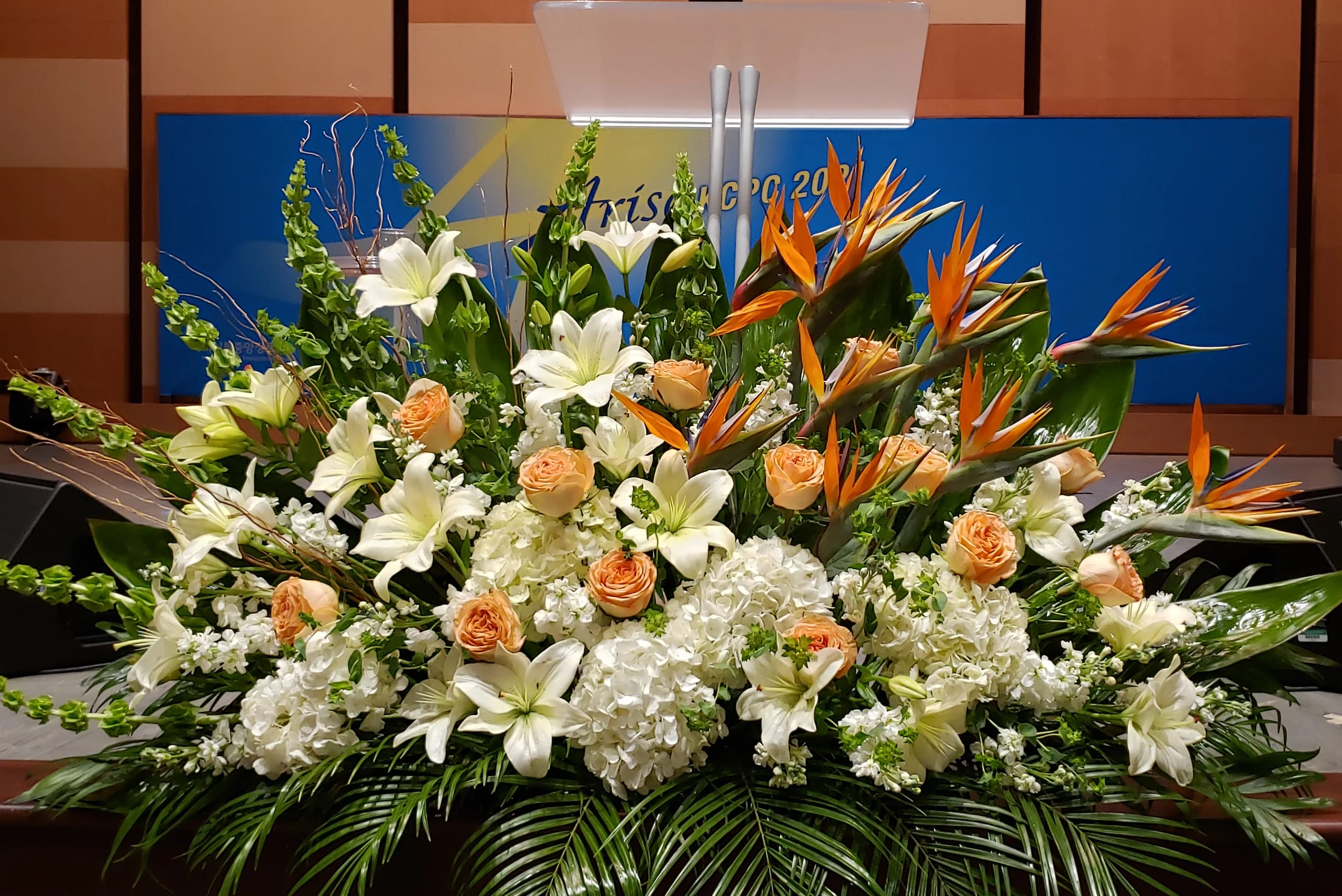 Large stage arrangement of white lilies, peach roses, Birds of Paradise, and white hydrangeas