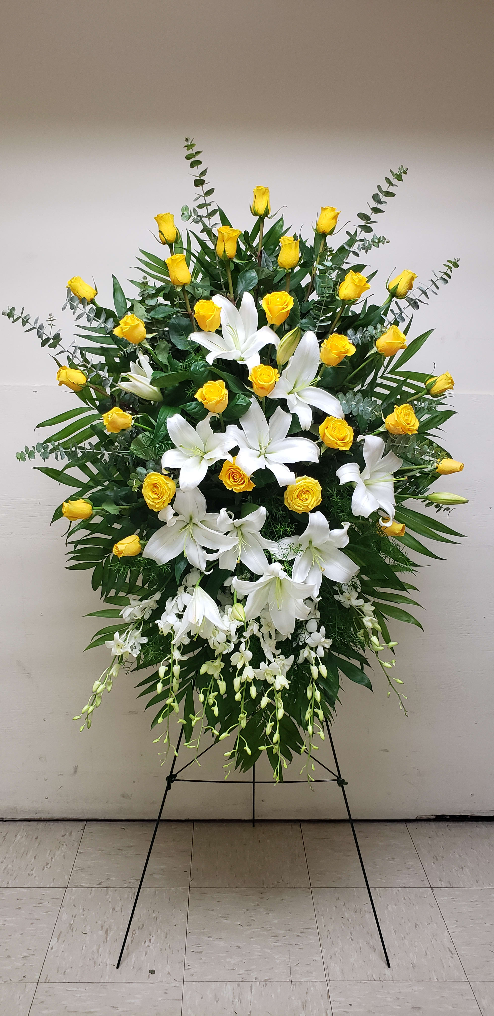 Standing spray of yellow roses and white lilies with cascading orchids on an easel