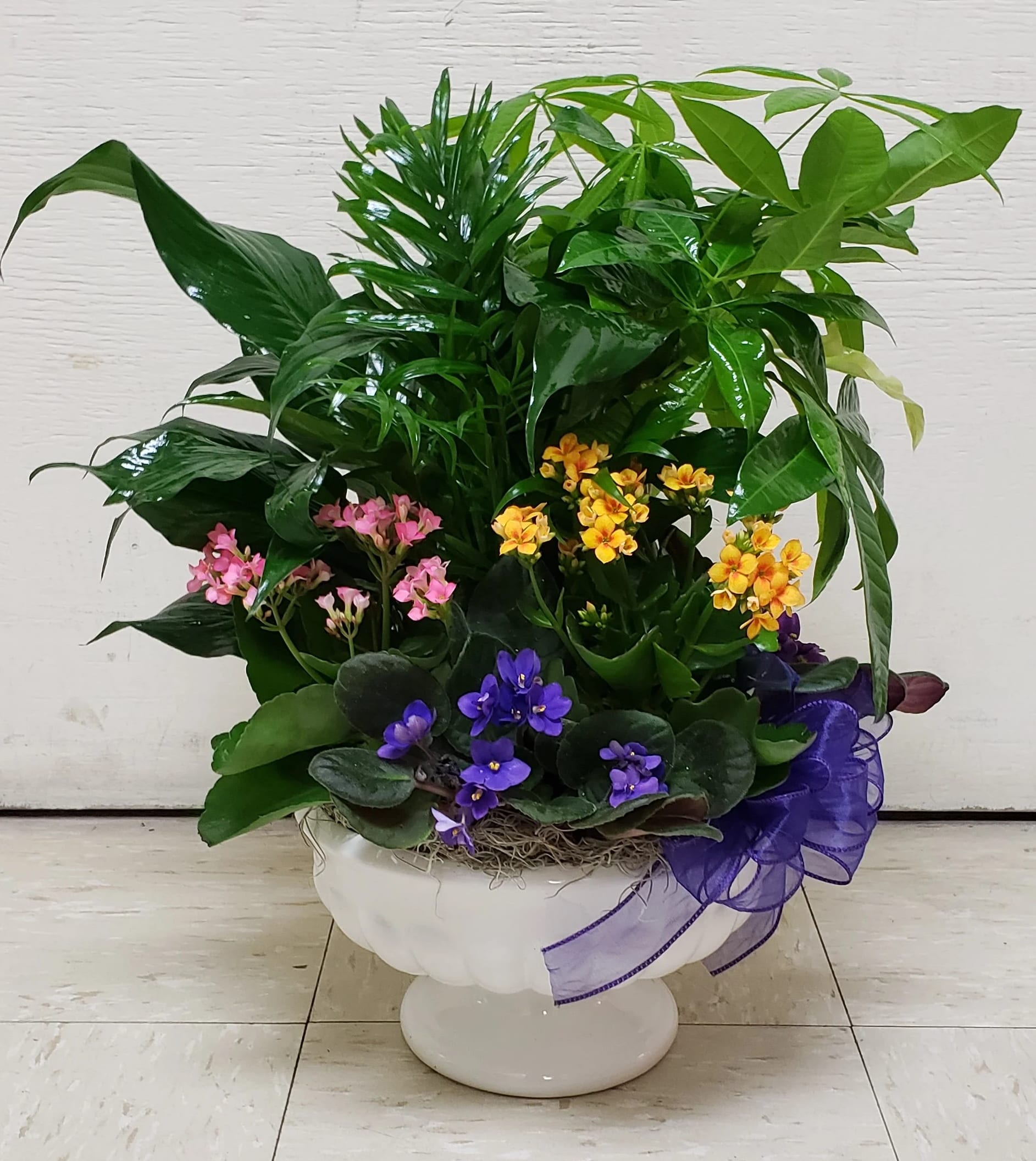 Mixed potted flowering plant arrangement in a white pedestal bowl