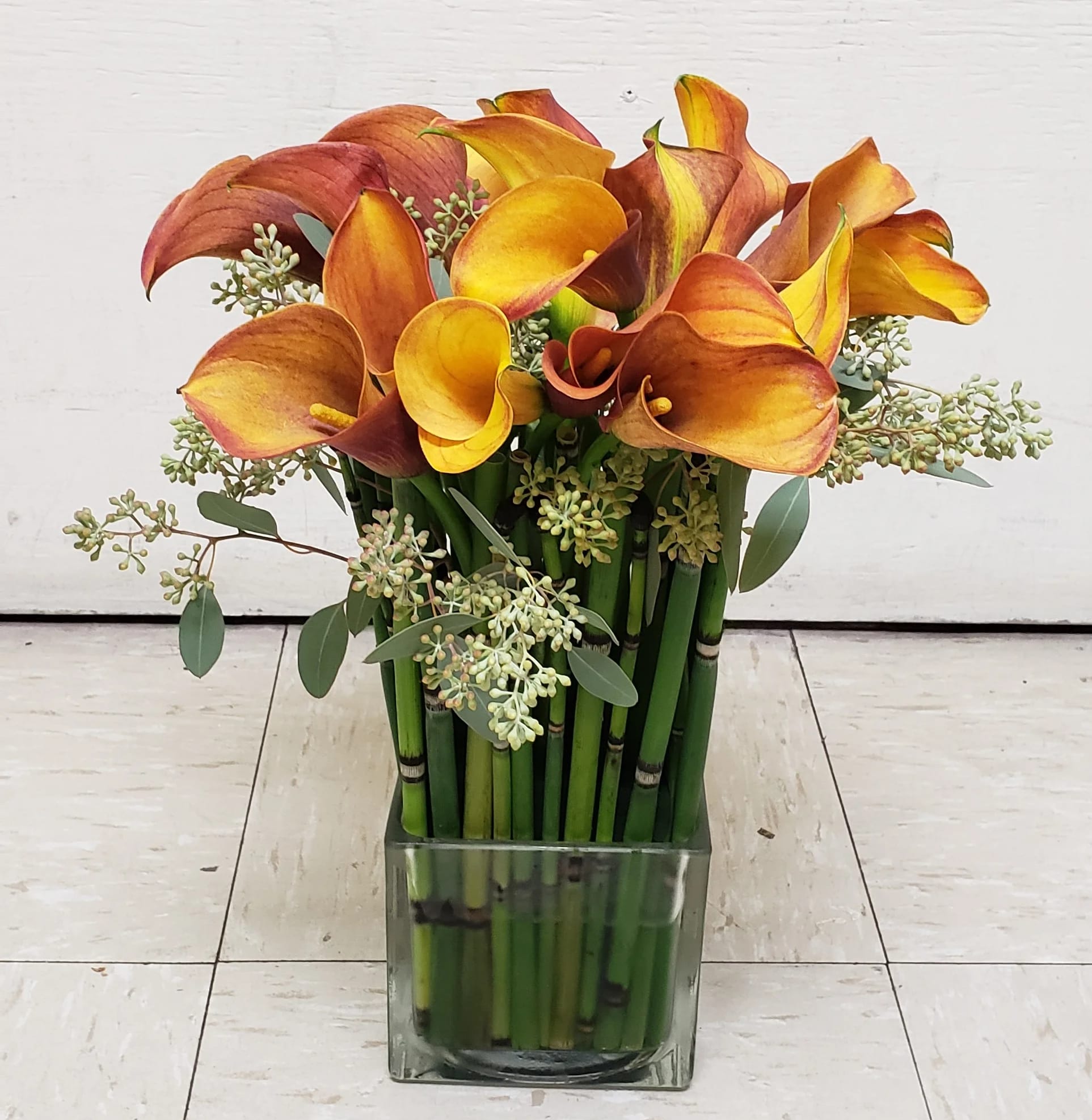 Orange and yellow calla lilies in a square glass vase