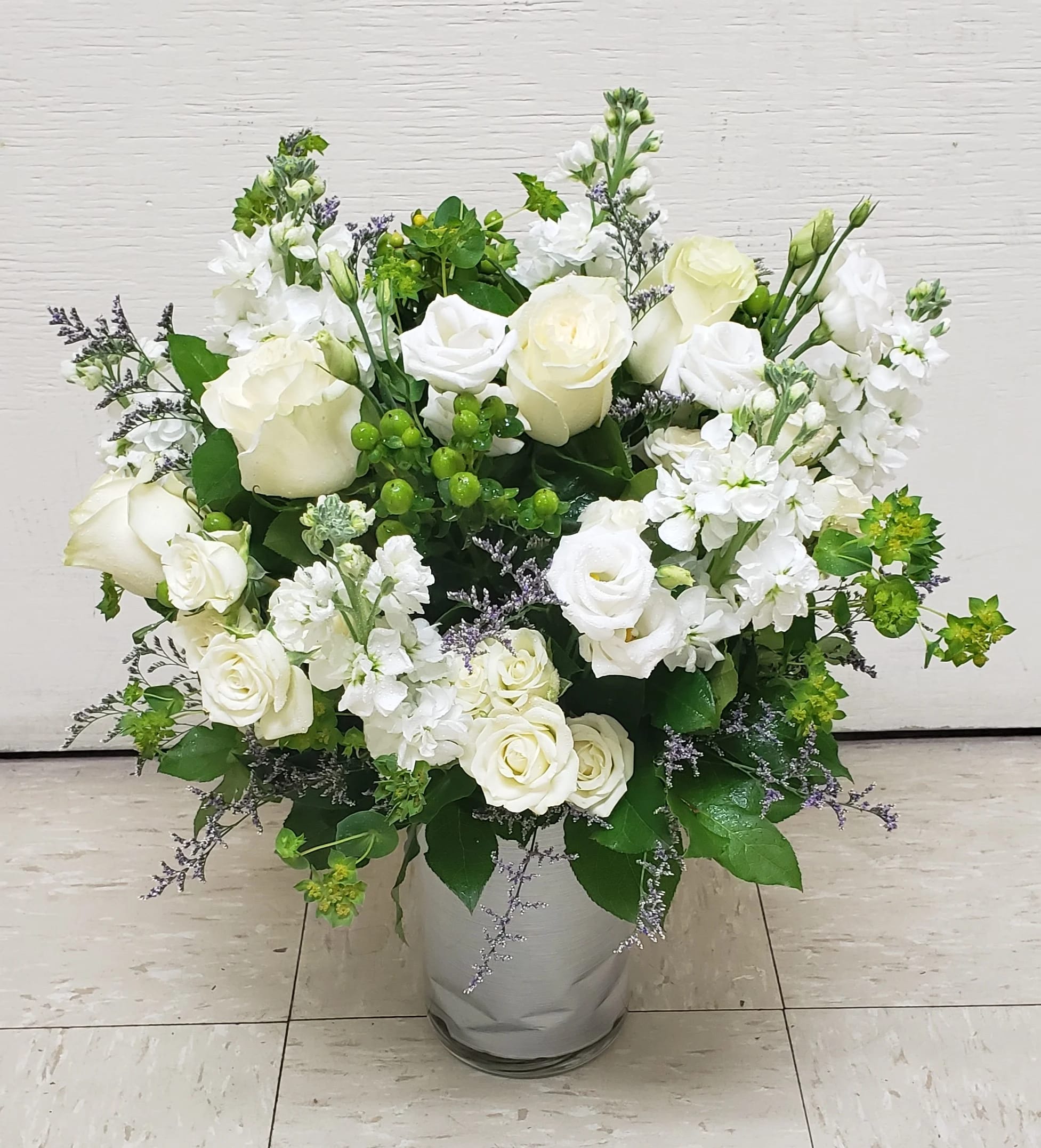 White roses and white stock in a glass vase with green accents