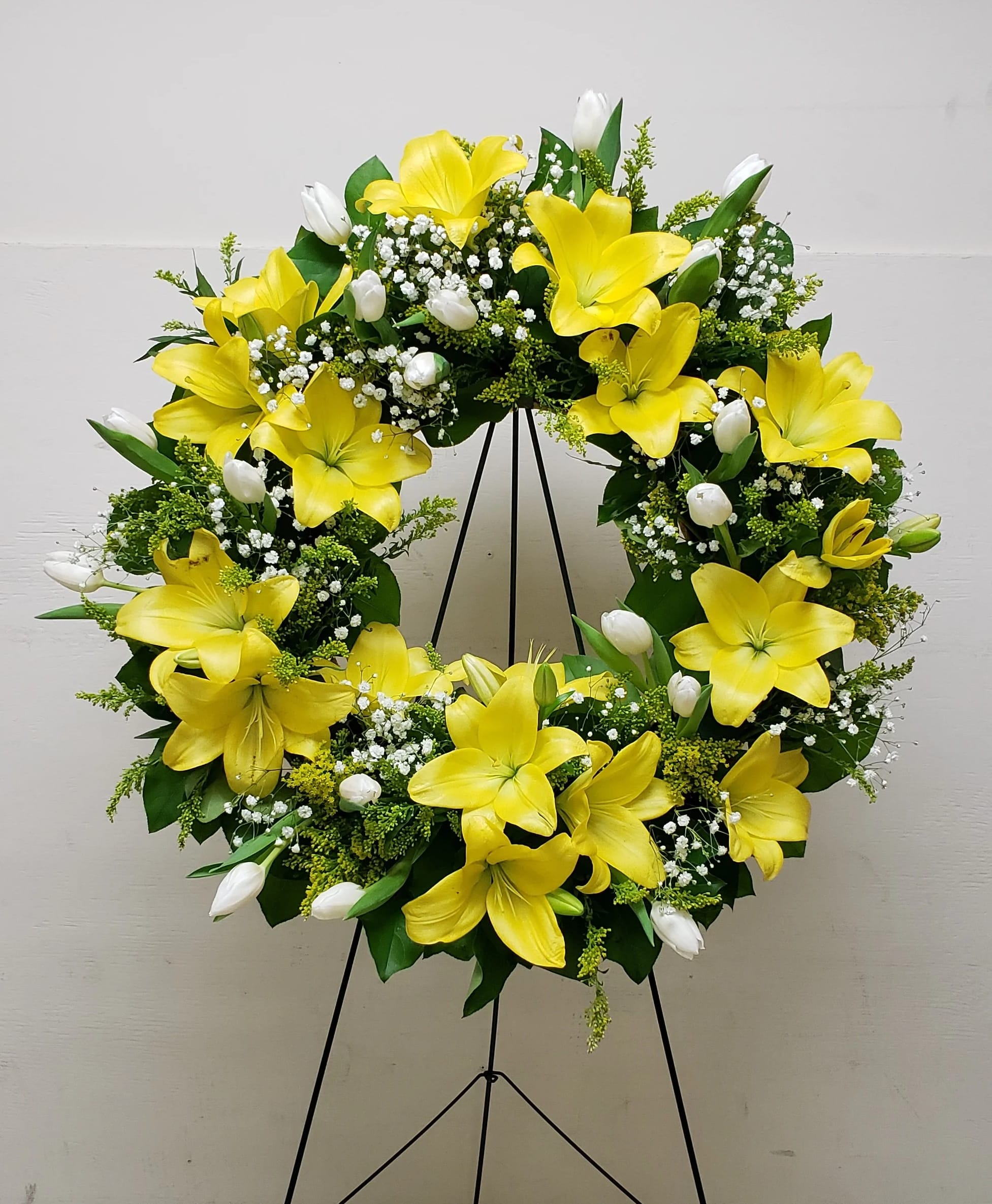 Standing wreath of yellow lilies and white tulips arranged in a ring on a metal easel