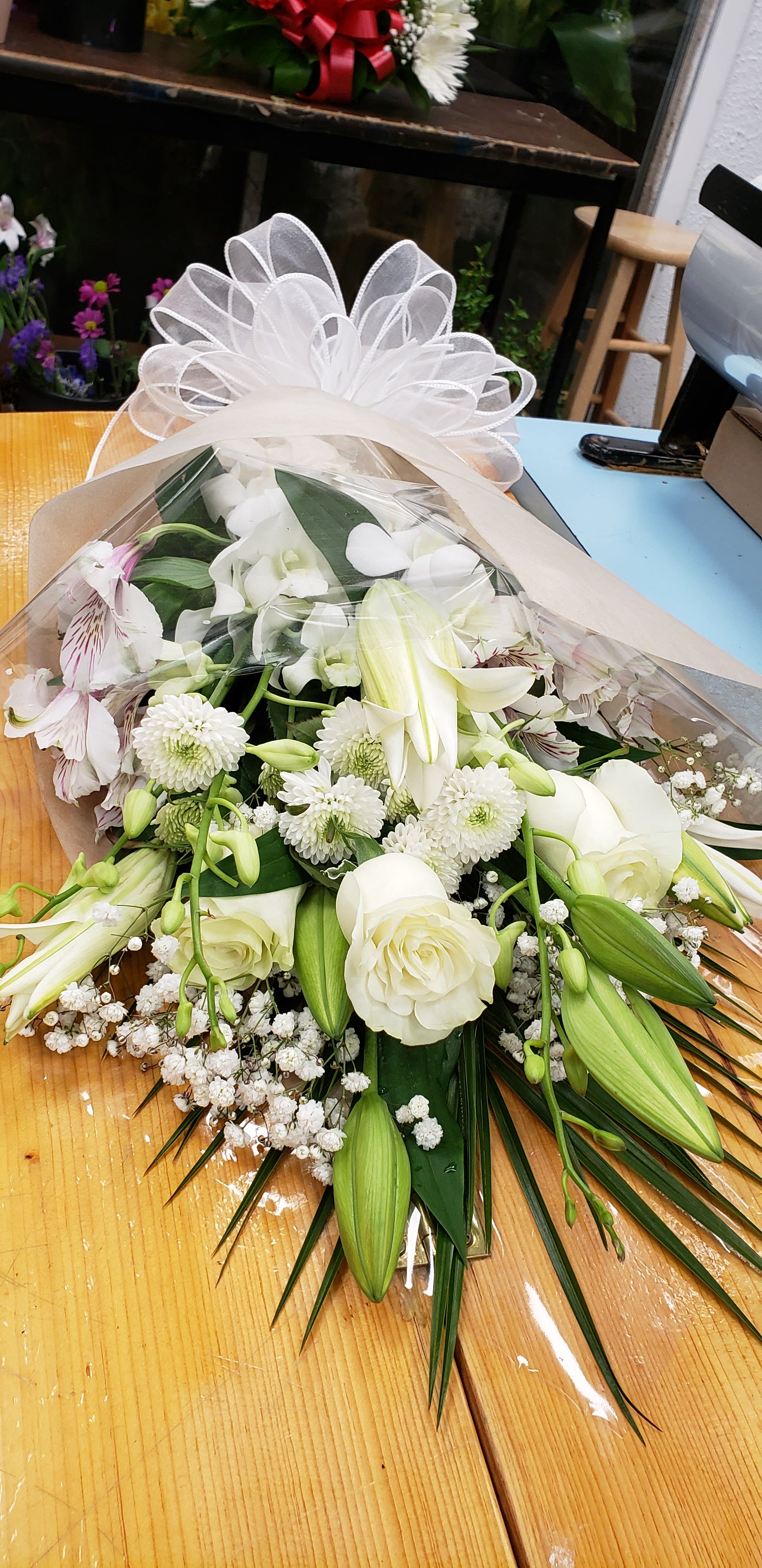 Wrapped bouquet of white roses, lilies, and chrysanthemums with a sheer bow on a wooden table