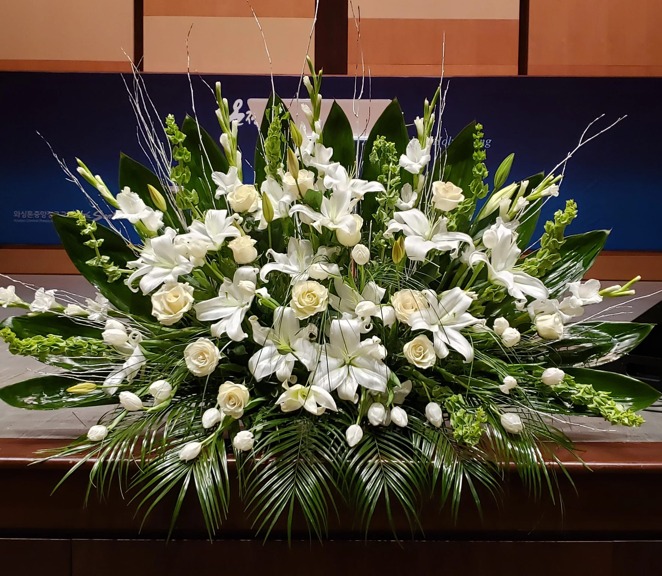 Large white lily and rose arrangement with tulips and Bells of Ireland in a low, fan-shaped design