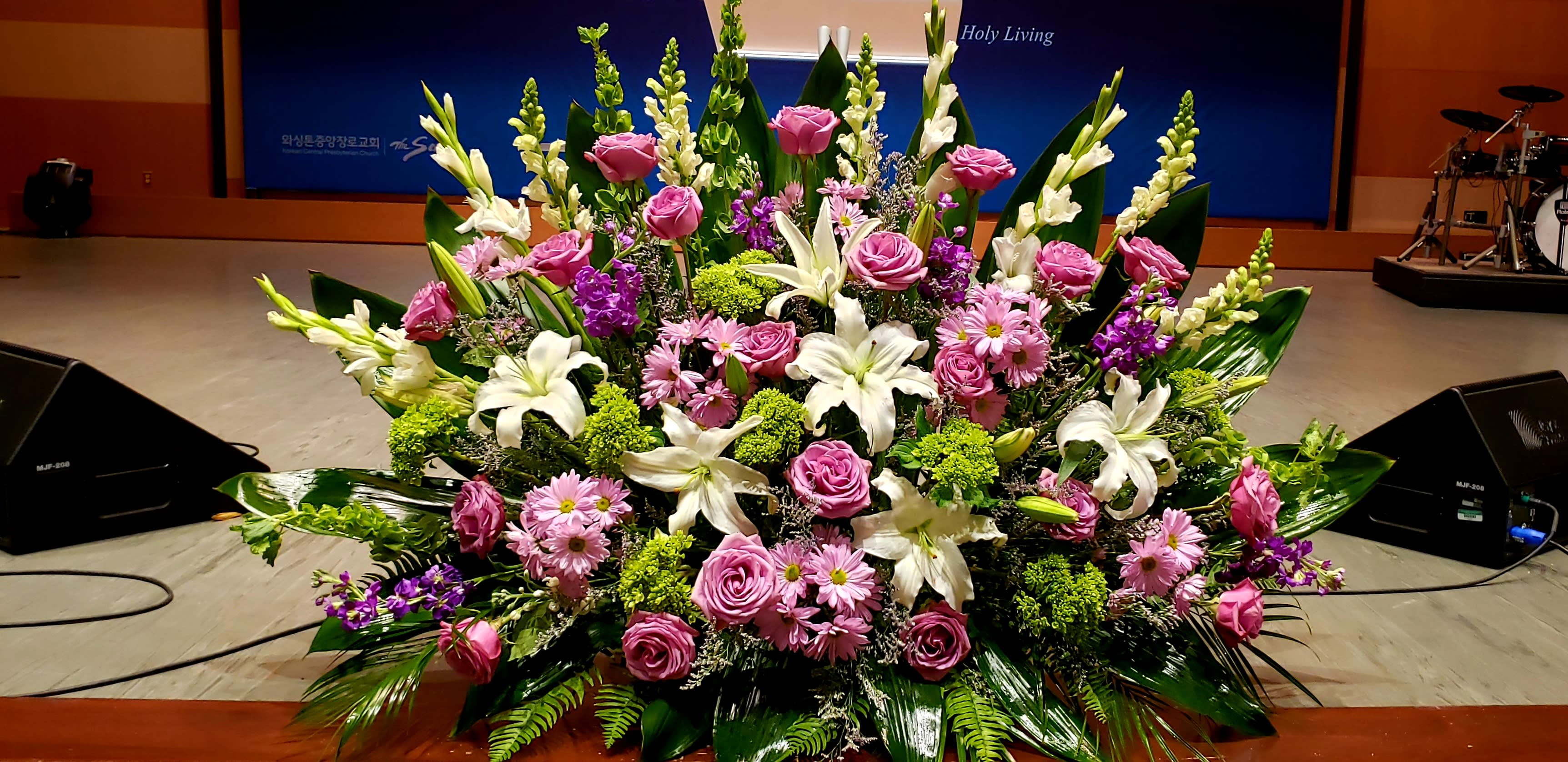 Large altar arrangement of white lilies, pink roses, and pink daisies with green and purple accents.
