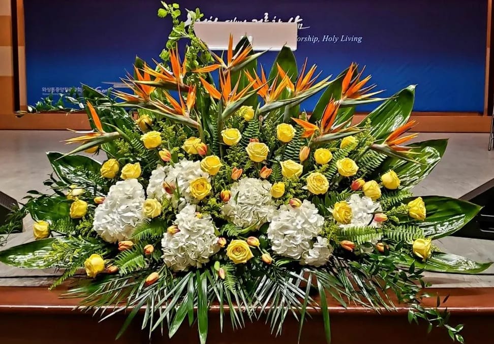 Large yellow and white floral stage arrangement with birds of paradise and tropical foliage