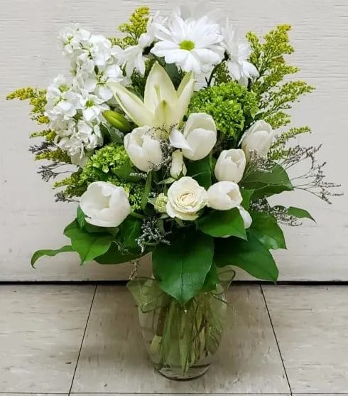 White floral arrangement in a clear glass vase with green accents