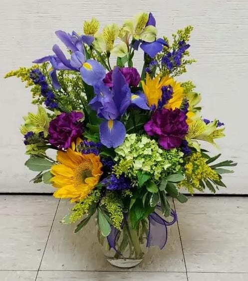 Mixed bouquet with purple, yellow, and blue flowers in a glass vase