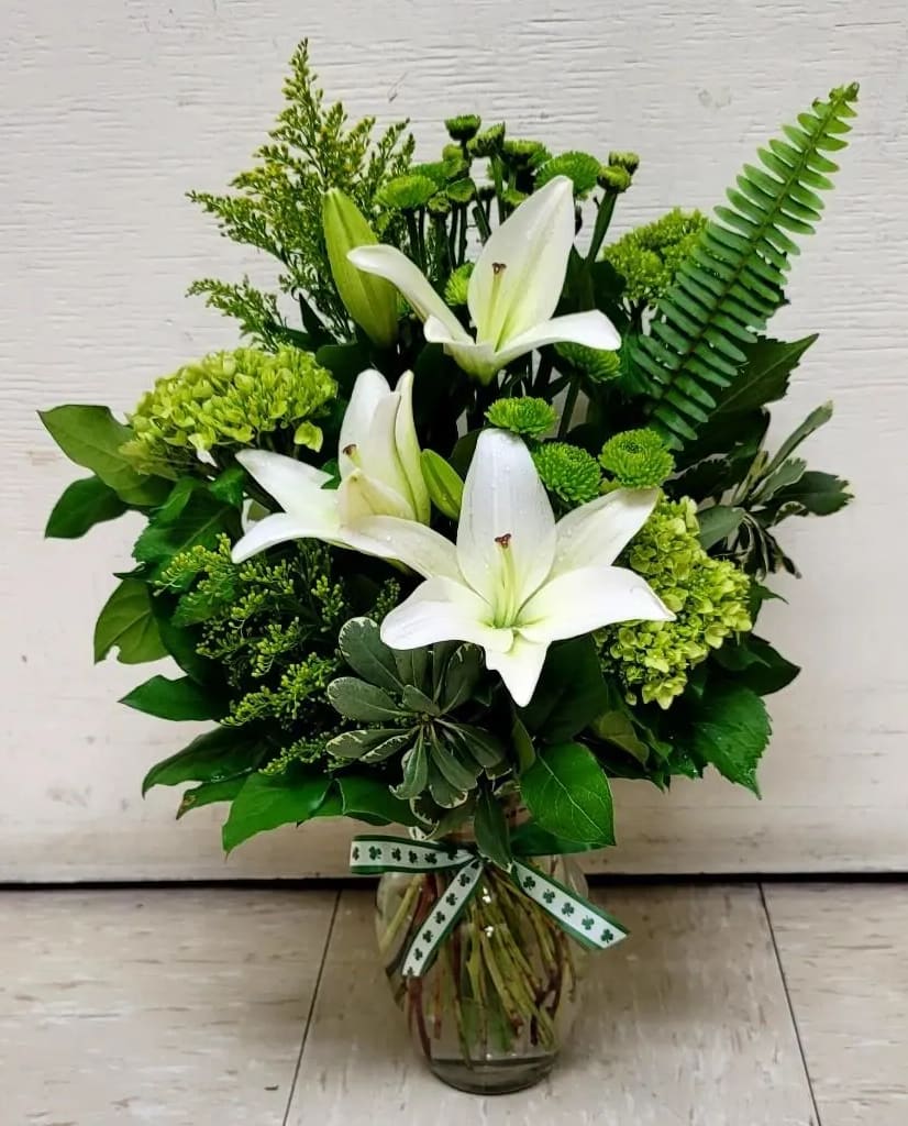 White lilies and green flowers arranged in a glass vase