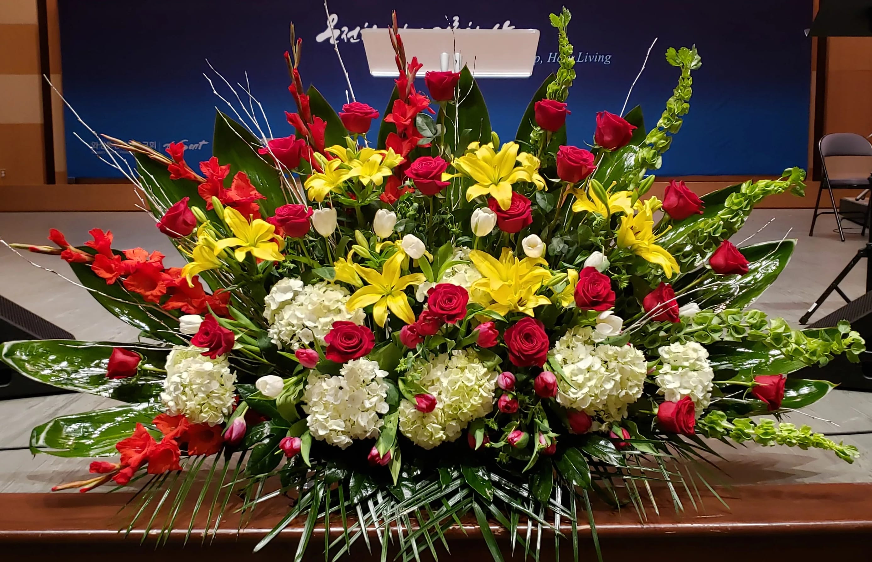 Large altar-style arrangement of red roses, yellow lilies, white hydrangeas, and tulips in a fan shape