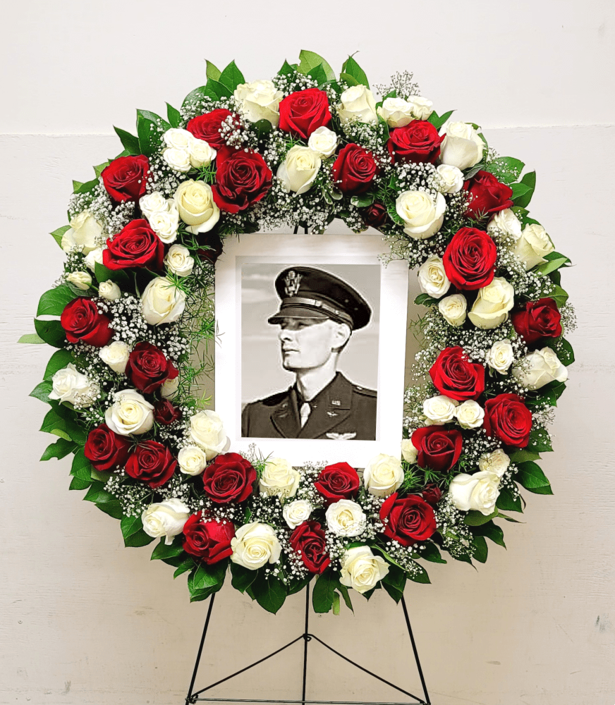 Standing circular wreath of red and white roses with baby’s breath framing a black-and-white portrait.