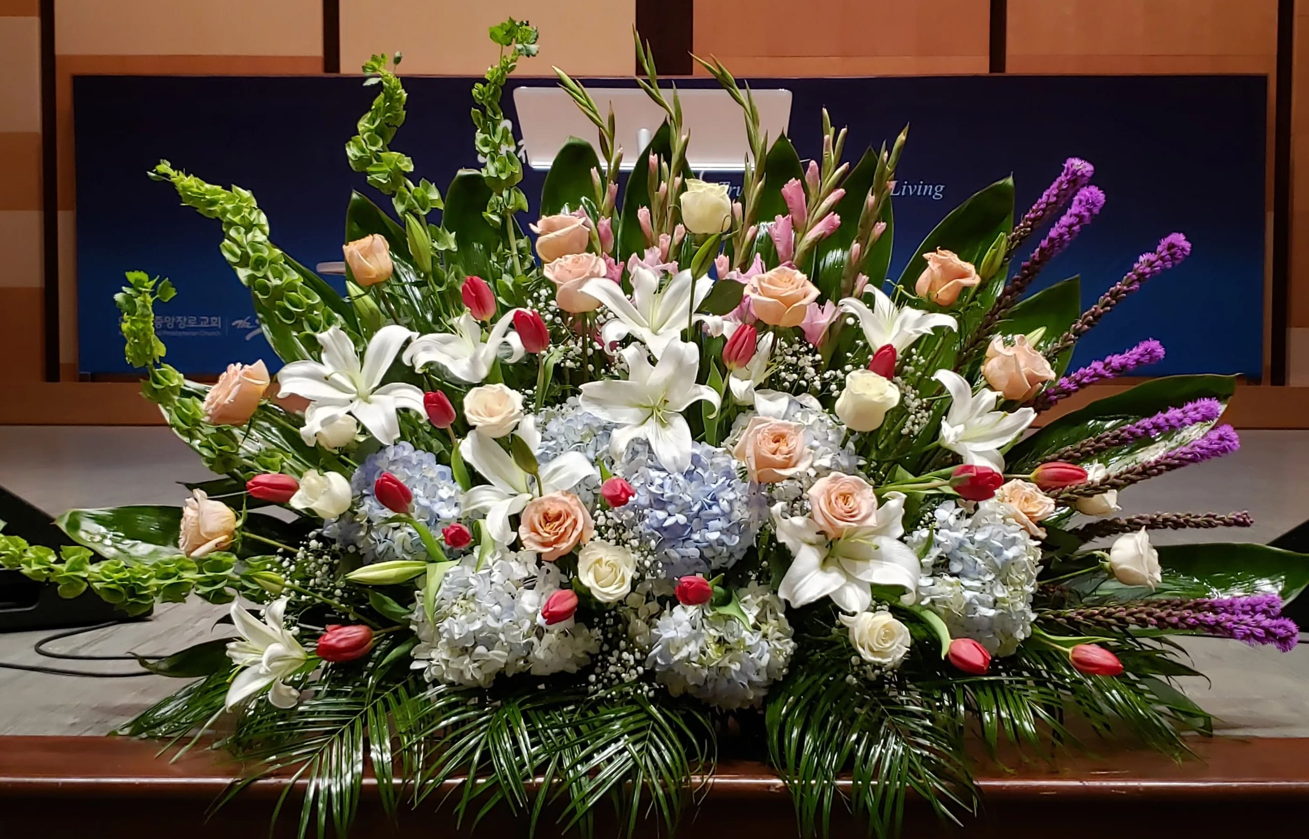 Large front-facing arrangement of white lilies, peach roses, blue hydrangeas, and pink tulips