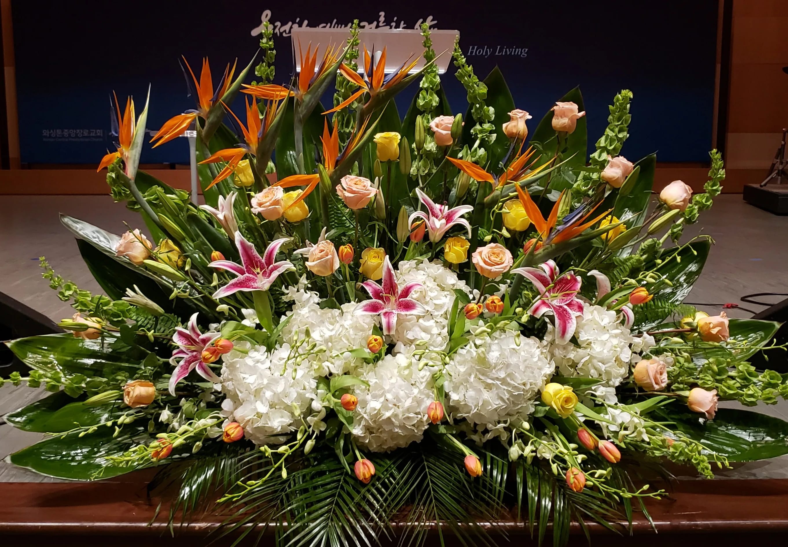 Large altar-style arrangement with white hydrangeas, pink lilies, roses, tulips, and birds of paradise
