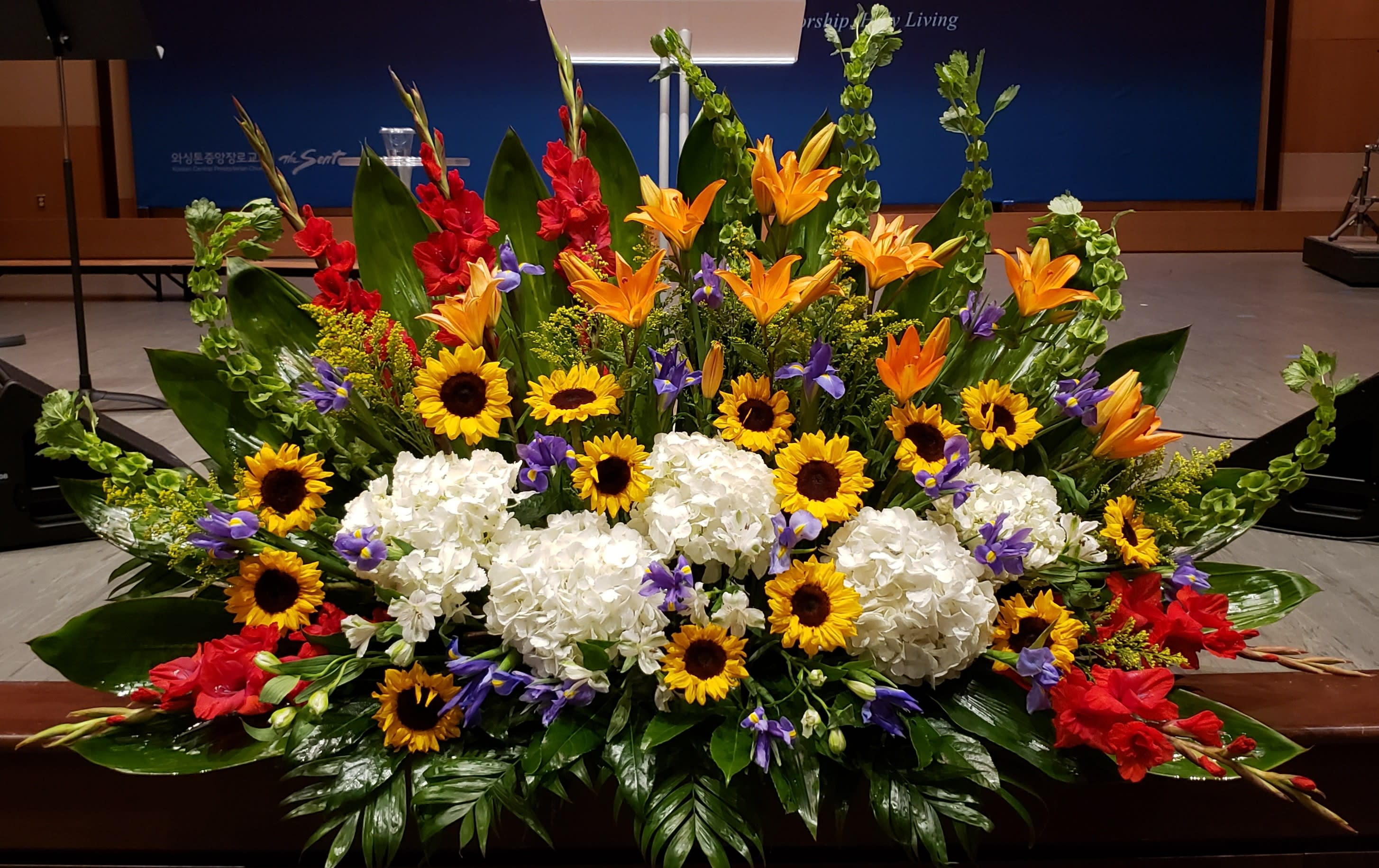 Large altar-style arrangement with sunflowers, white hydrangeas, orange lilies and mixed bright flowers