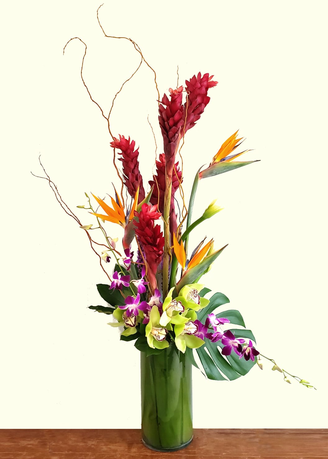 Tall tropical arrangement with orchids and bird of paradise in a glass vase