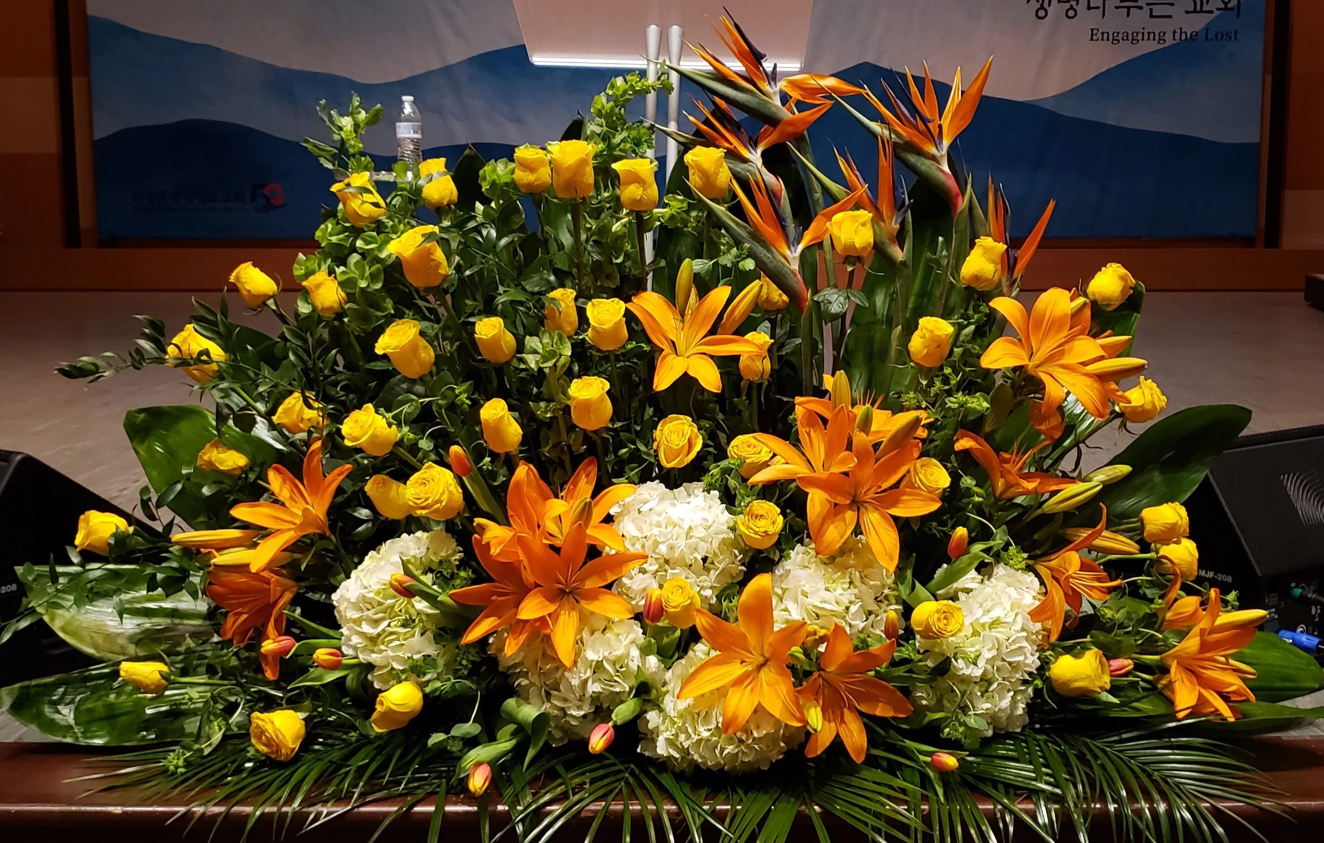 Large altar arrangement of orange lilies, yellow roses, tropical blooms and white hydrangeas.