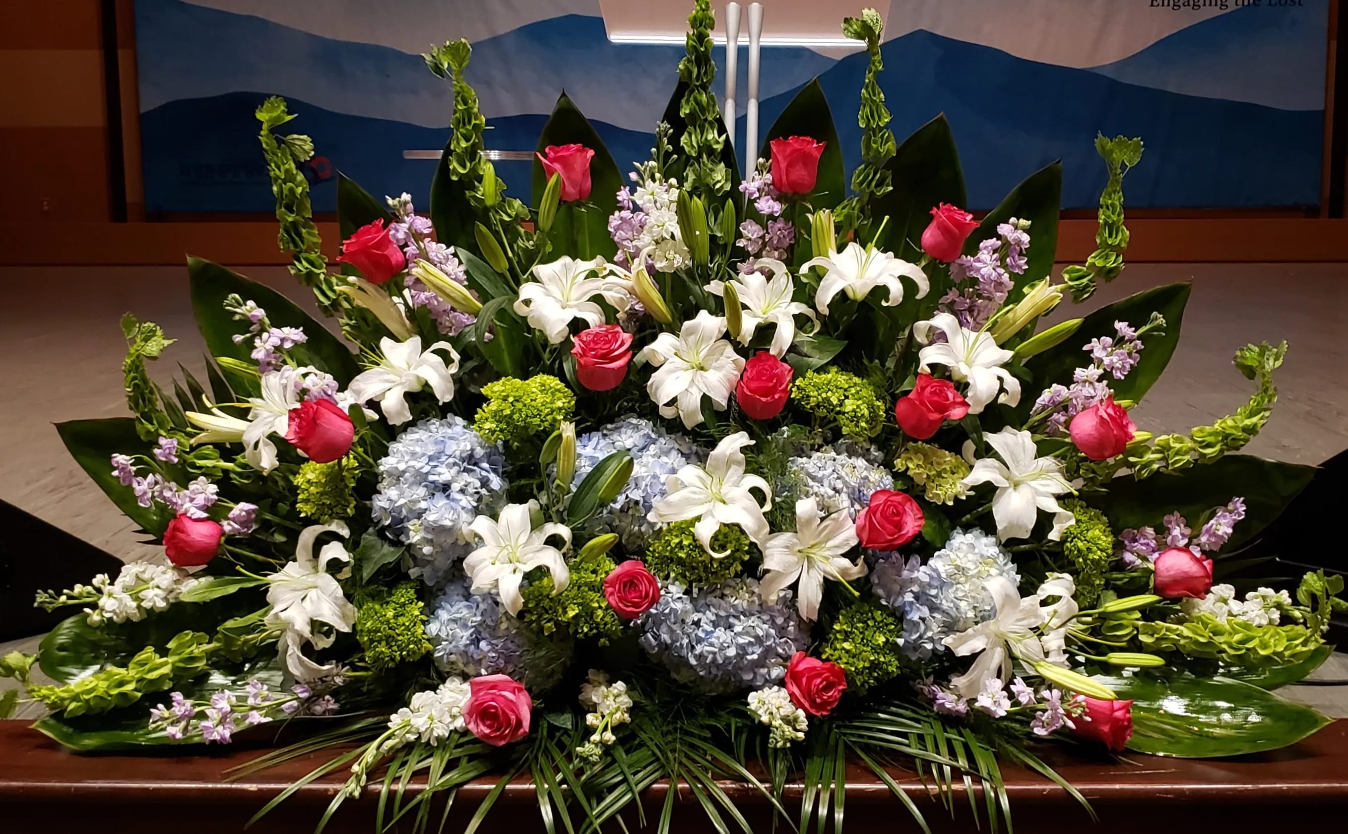 Large altar arrangement with white lilies, pink roses, blue hydrangeas, and green accents