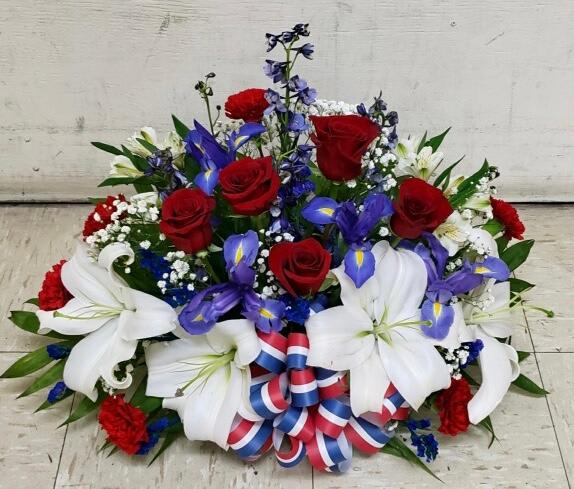 Patriotic red, white, and blue floral arrangement with roses, lilies, and ribbon bow