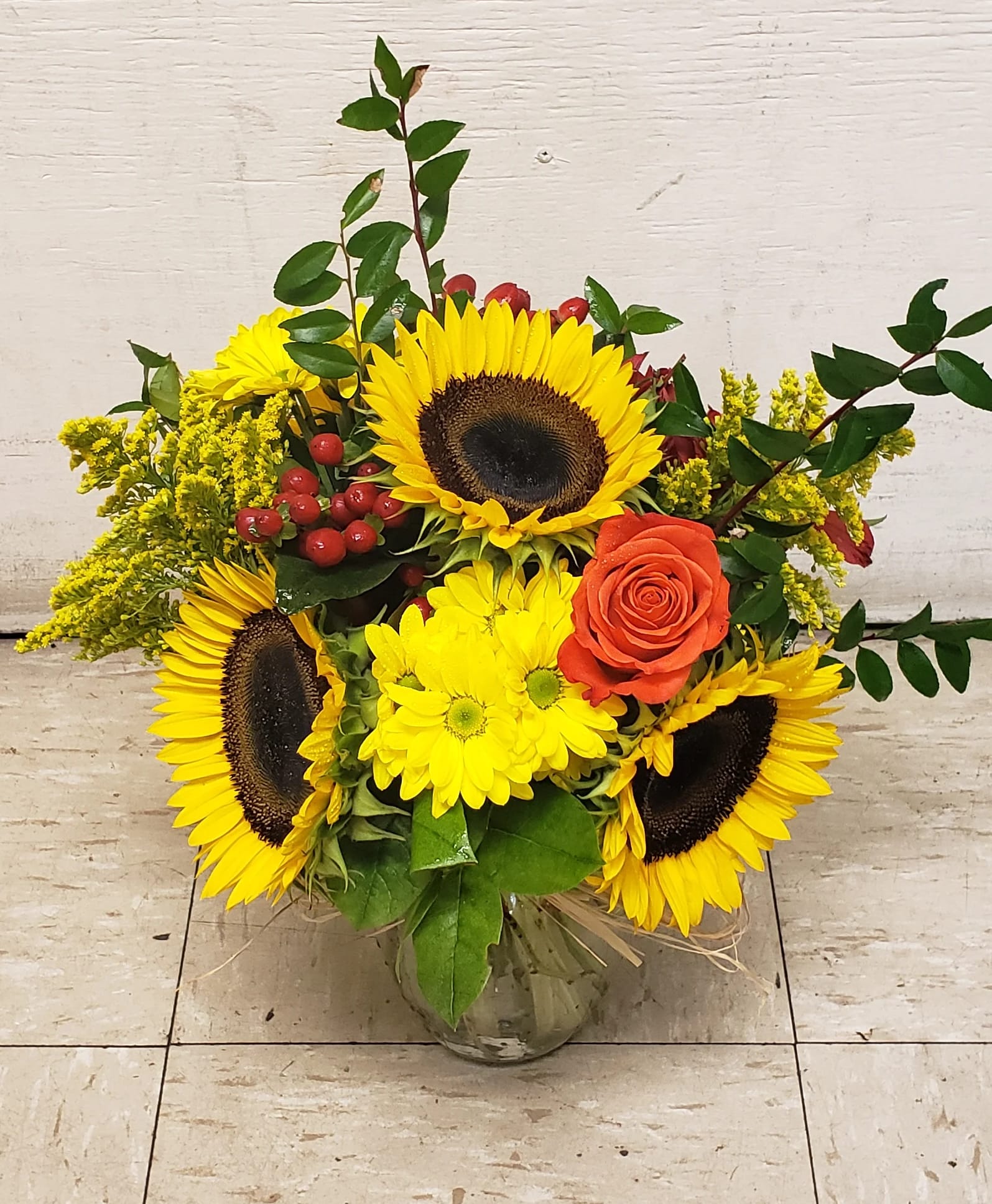 Sunflower and orange rose arrangement in a glass vase