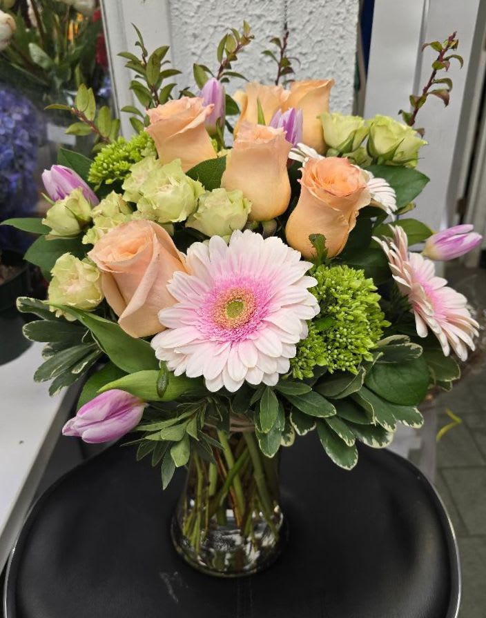 Bouquet of peach roses, pink gerbera daisies, and purple tulips in a glass vase