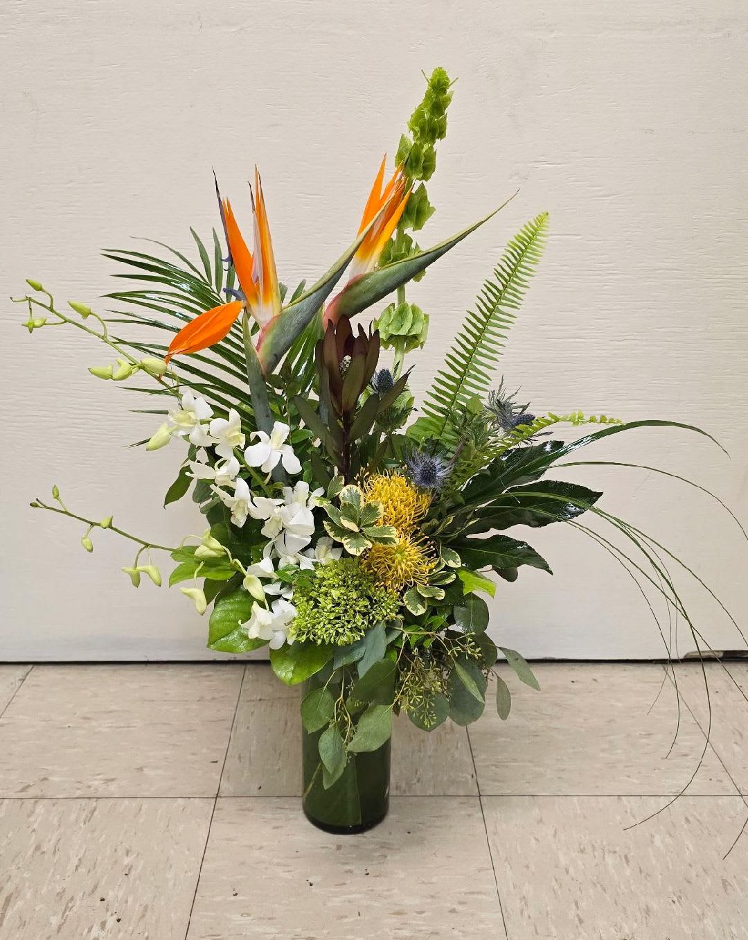 Tall tropical arrangement with orange bird-of-paradise and white orchids in a glass vase