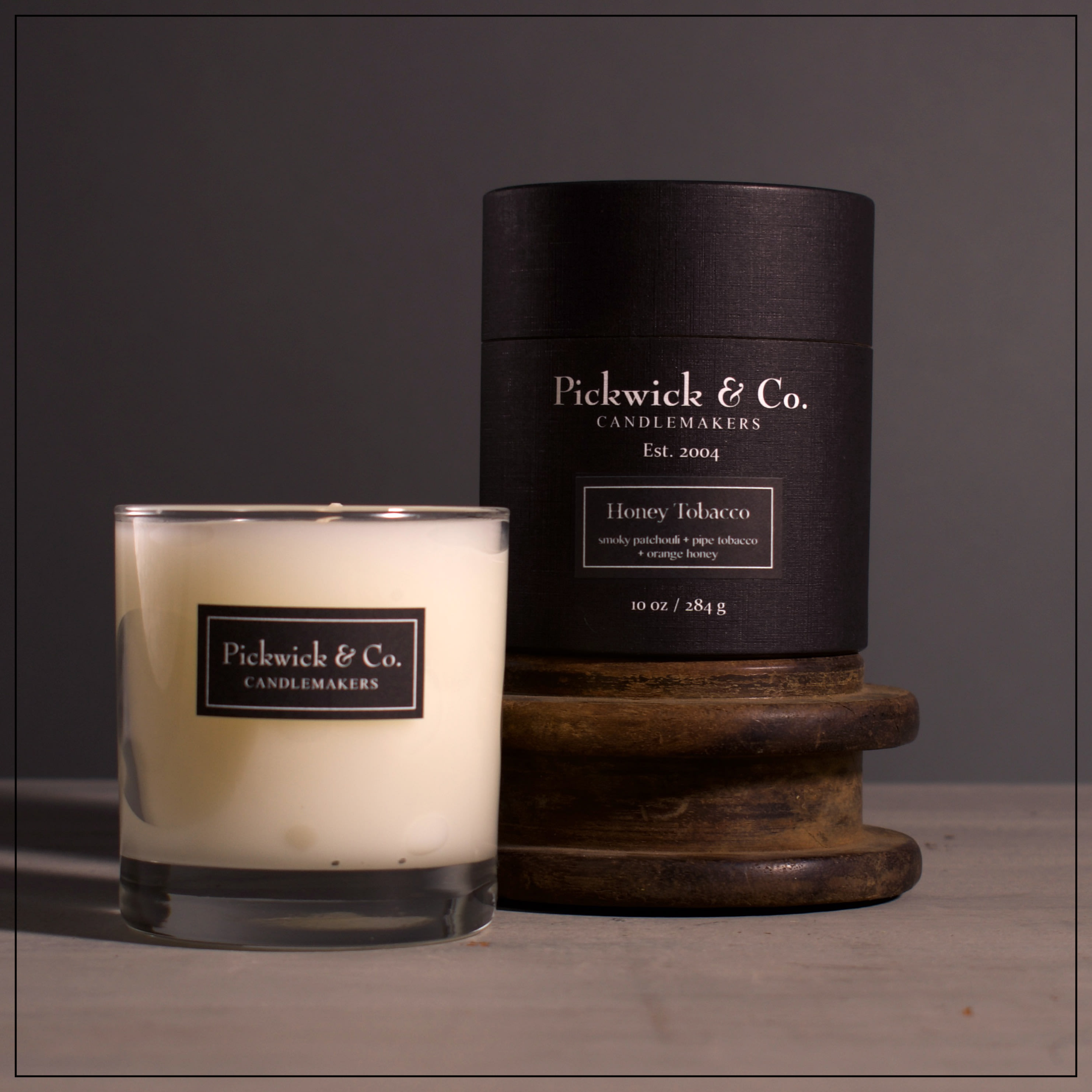 Two scented candles, one in a glass tumbler and one in a black box