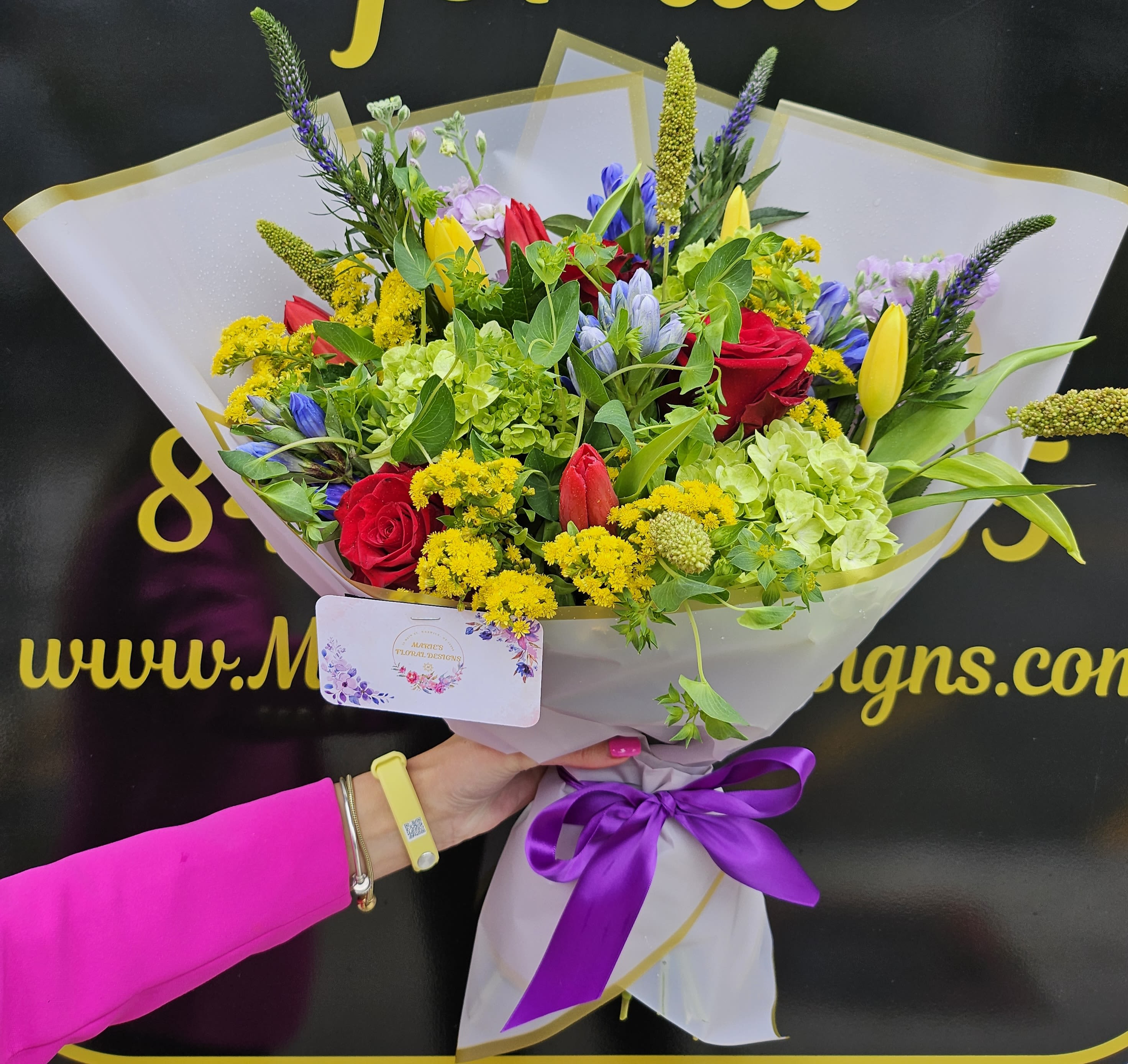 Bouquet of red roses, yellow tulips, and green hydrangeas wrapped in white paper