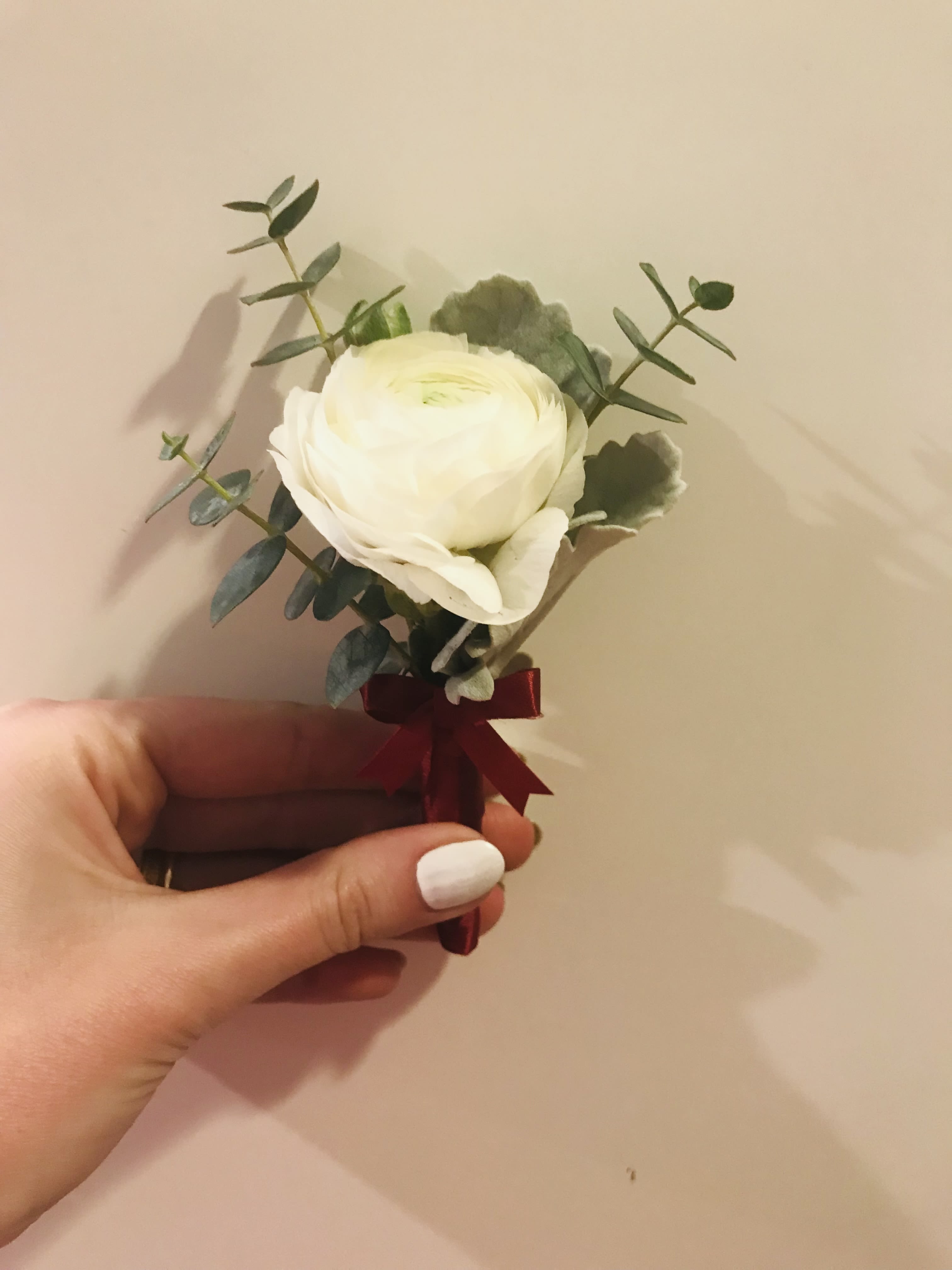 Small white flower boutonniere with greenery and a burgundy ribbon