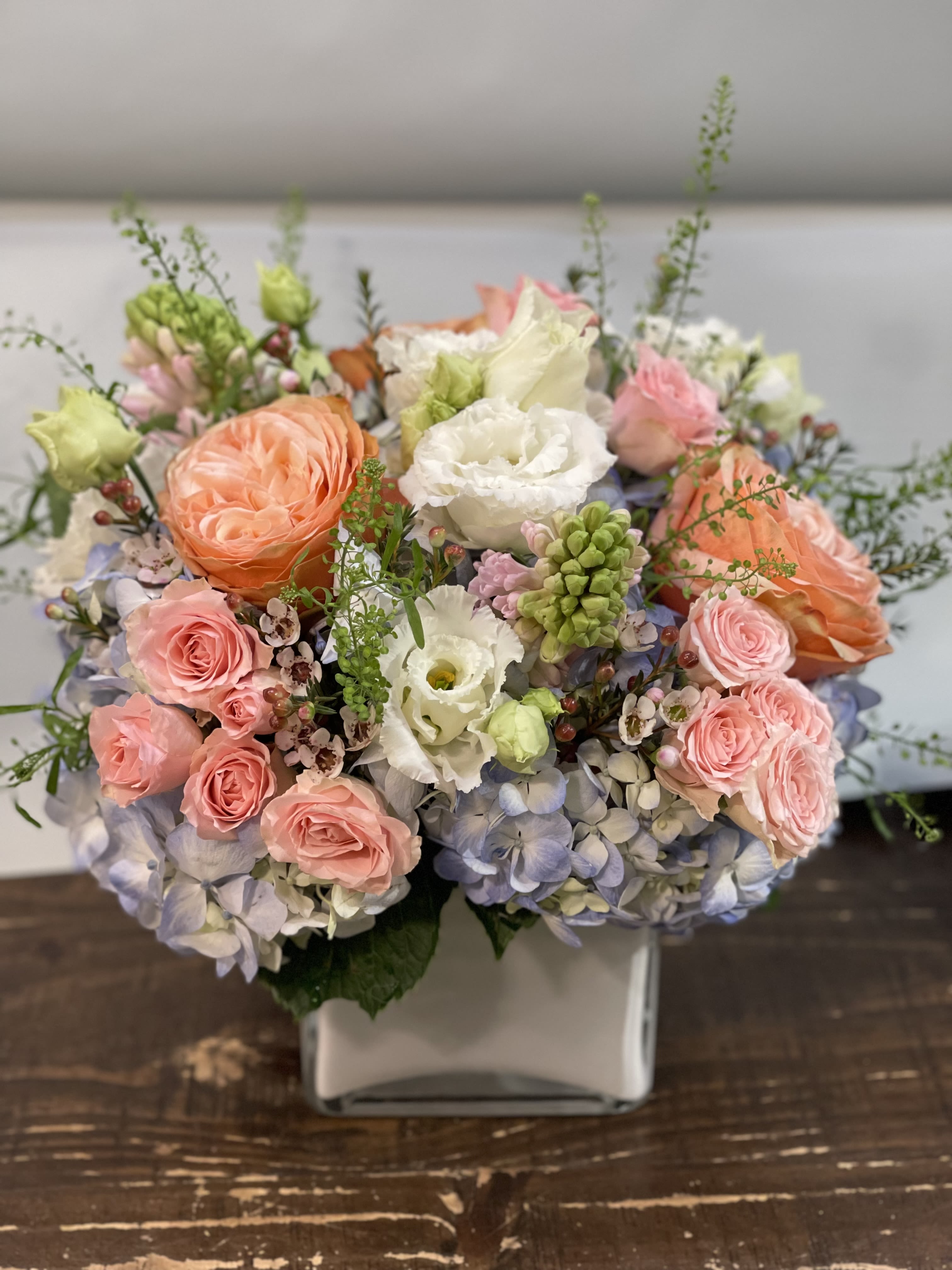 Pastel bouquet of roses, hydrangeas, and white blooms in a square vase