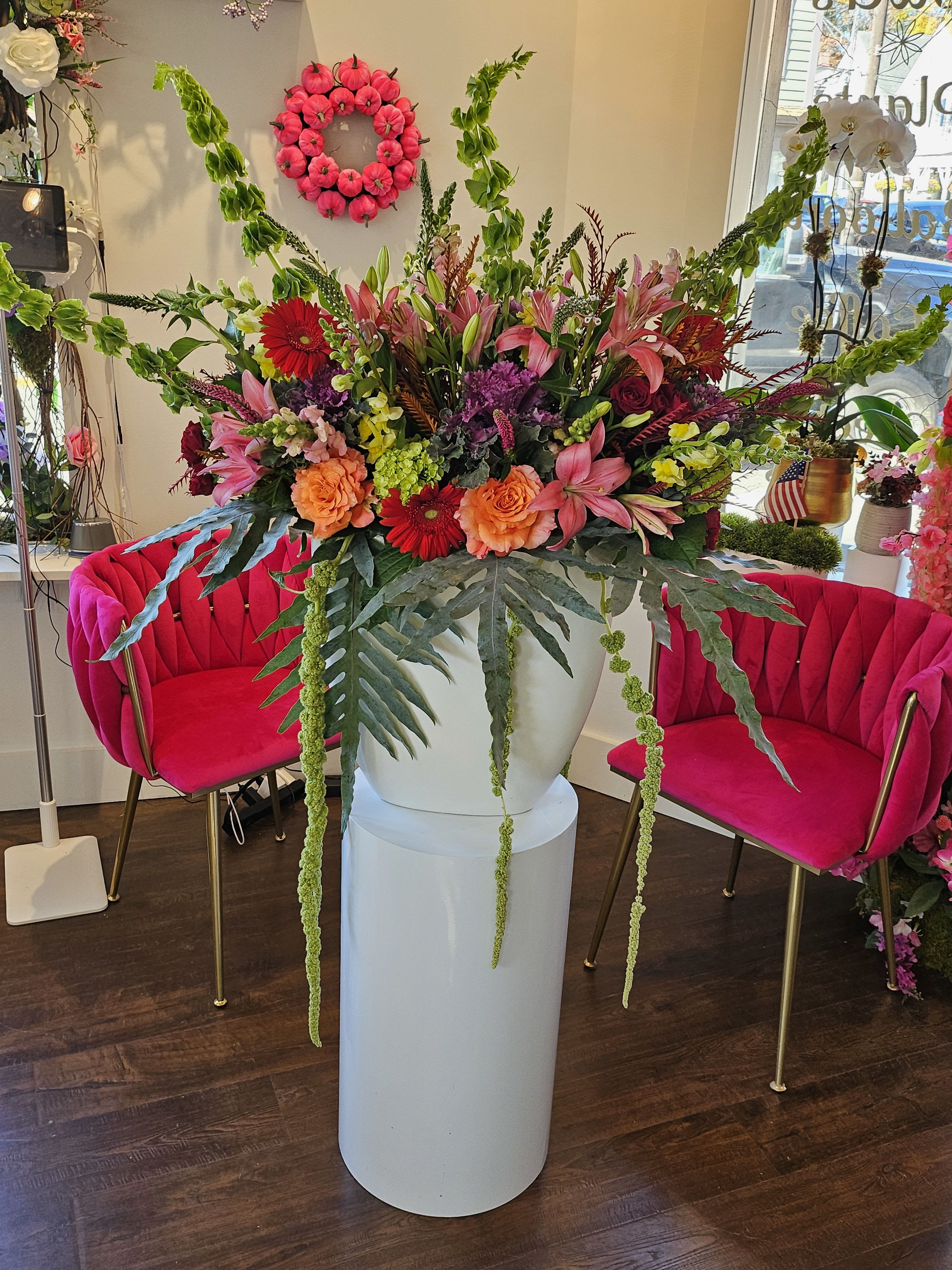 Large mixed flower arrangement in a white pedestal vase with pink and orange blooms