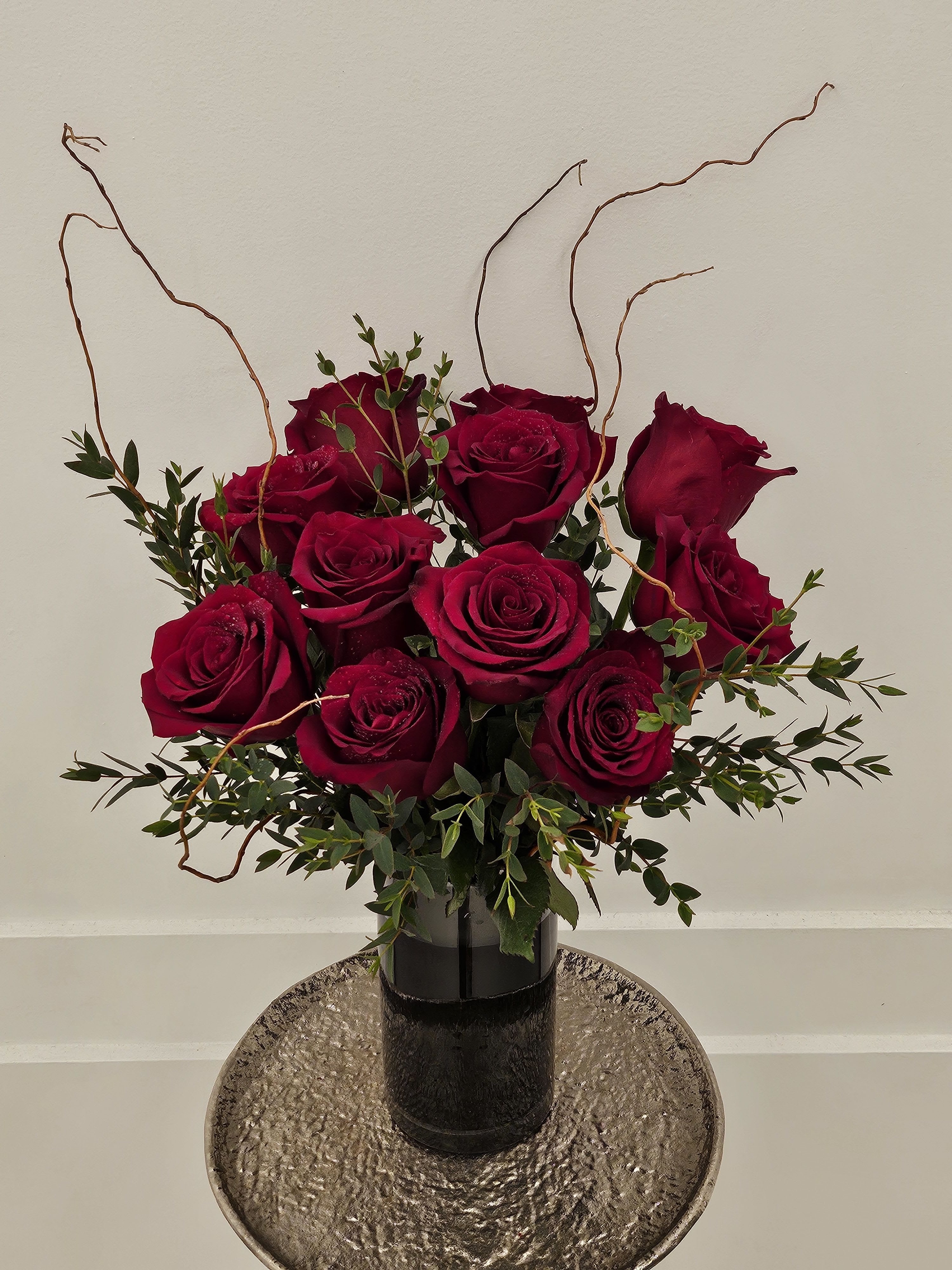 Deep red roses arranged in a black vase with curly branches