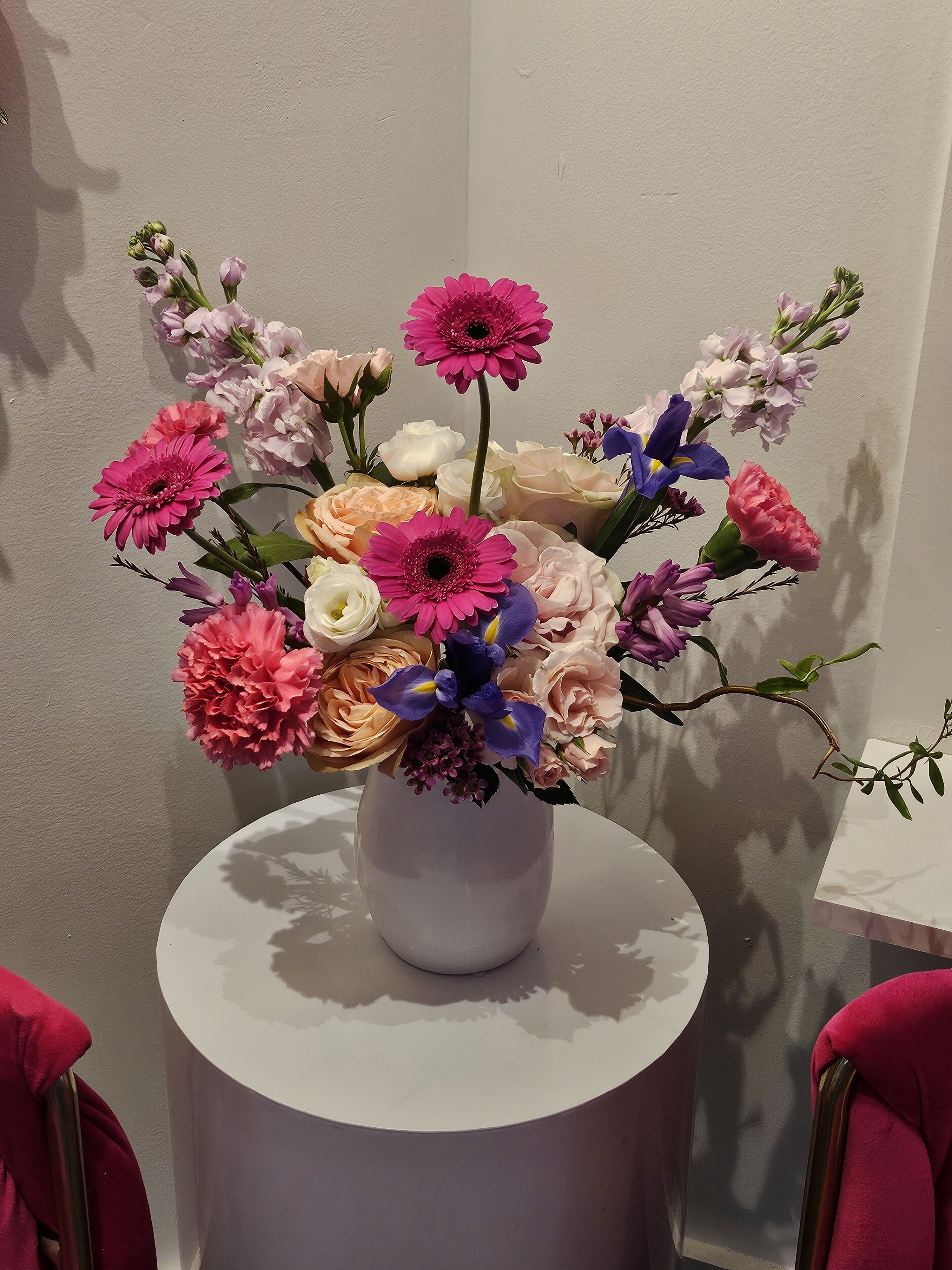 Mixed bouquet of pink, peach, white, and purple flowers in a white vase
