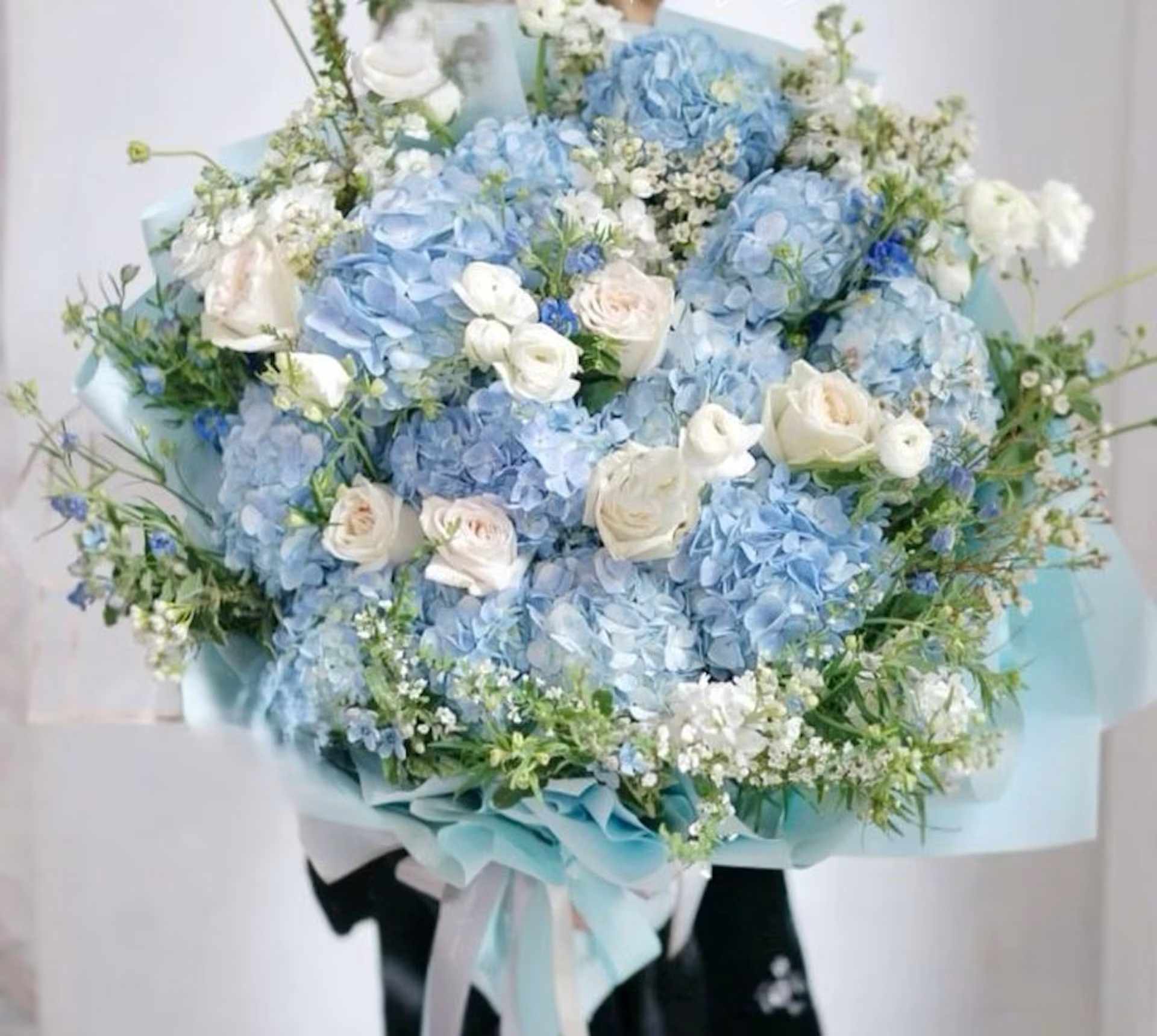 Large bouquet of blue hydrangeas and white roses wrapped in pale blue paper