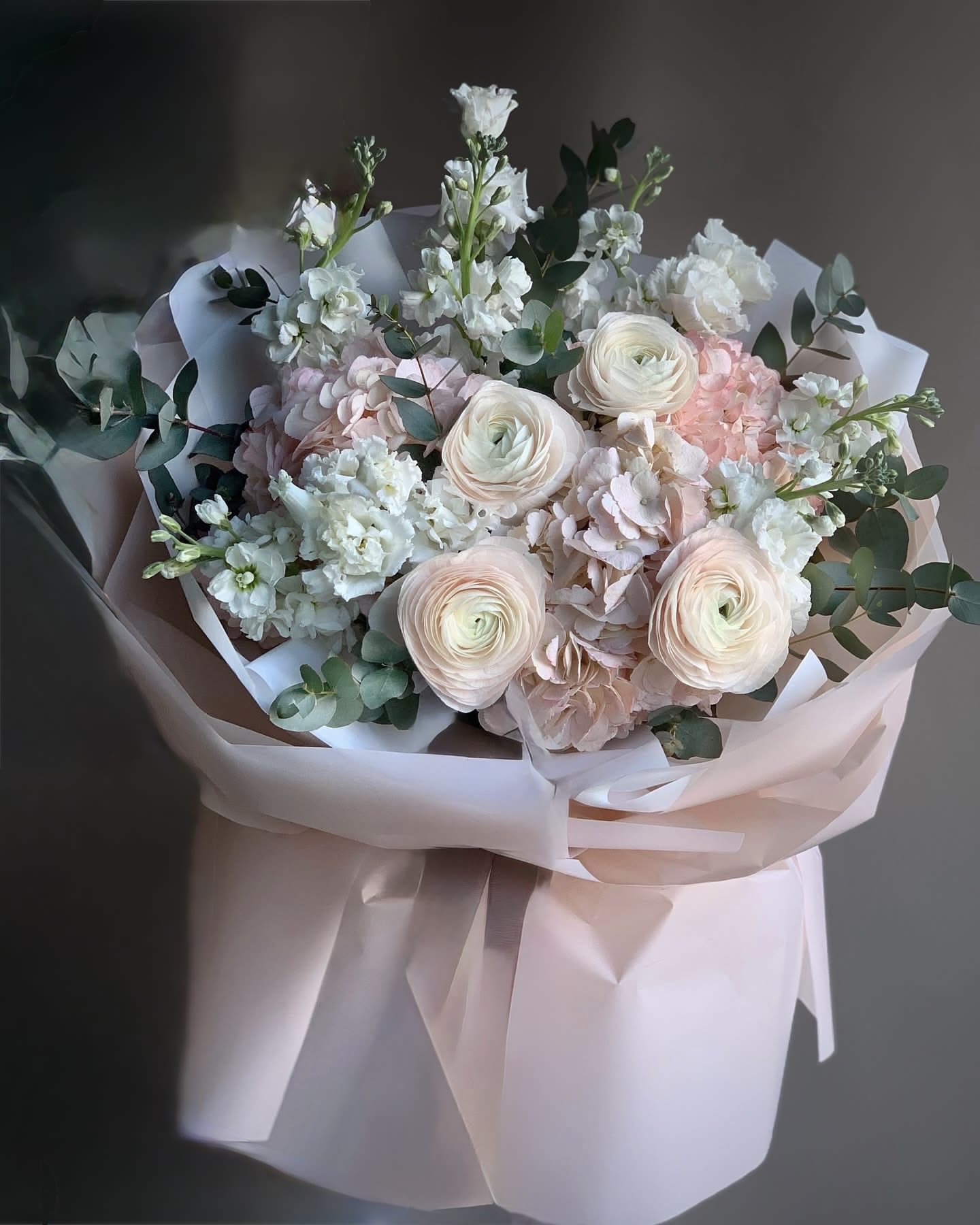 Pastel bouquet of white and blush flowers wrapped in pale pink paper