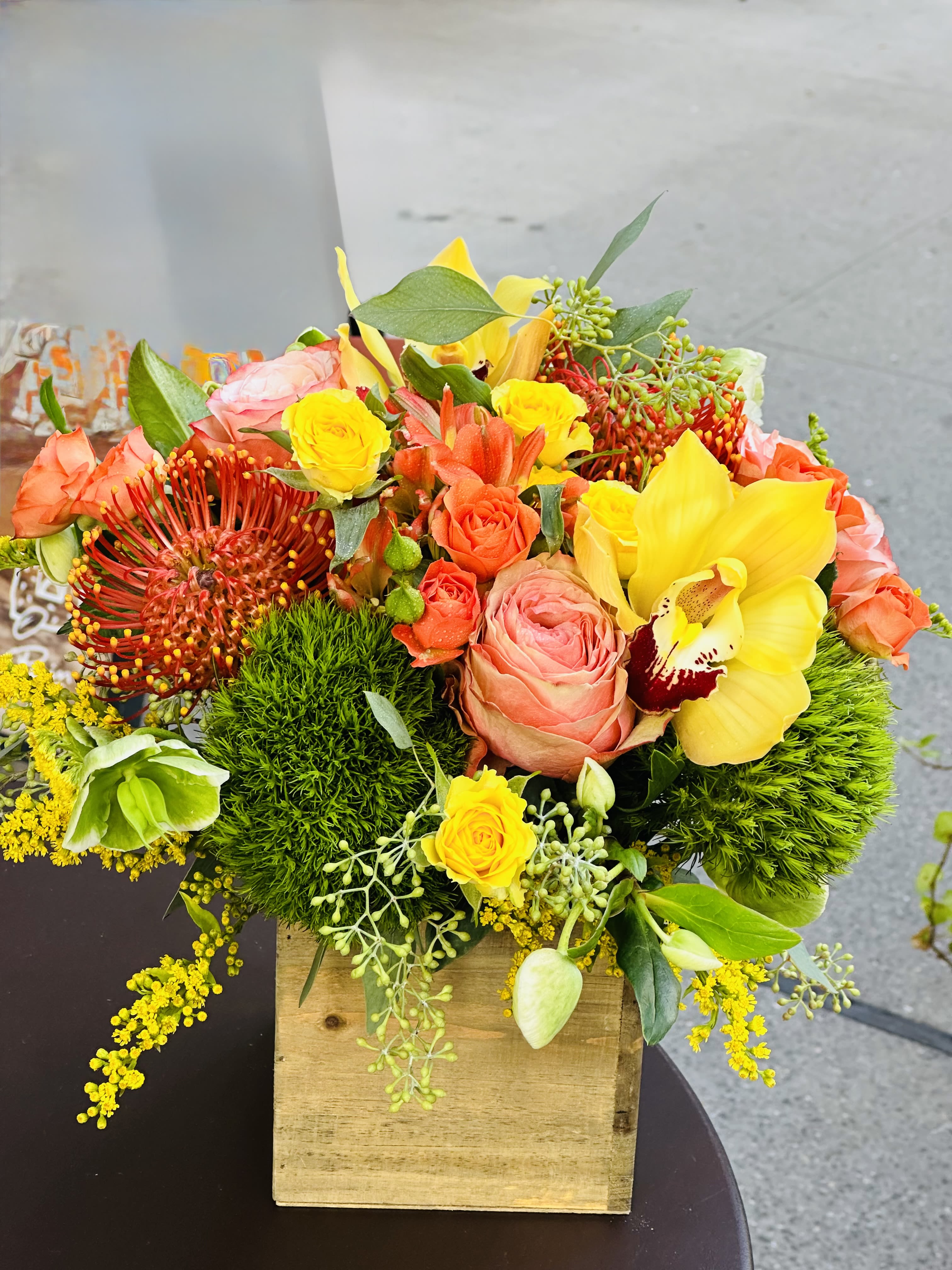 Bright mixed bouquet in a wooden box with yellow, orange, and pink blooms