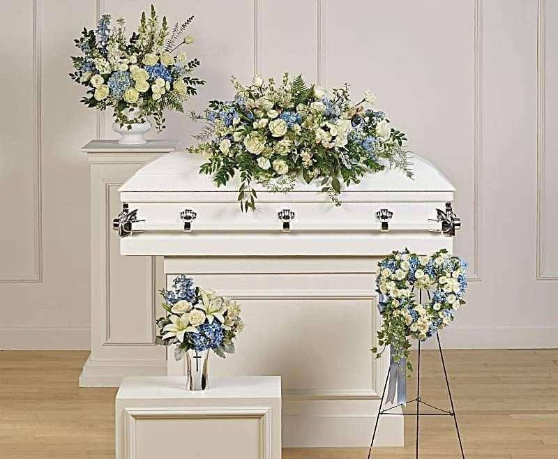 White casket with blue and cream floral sprays in a funeral setting