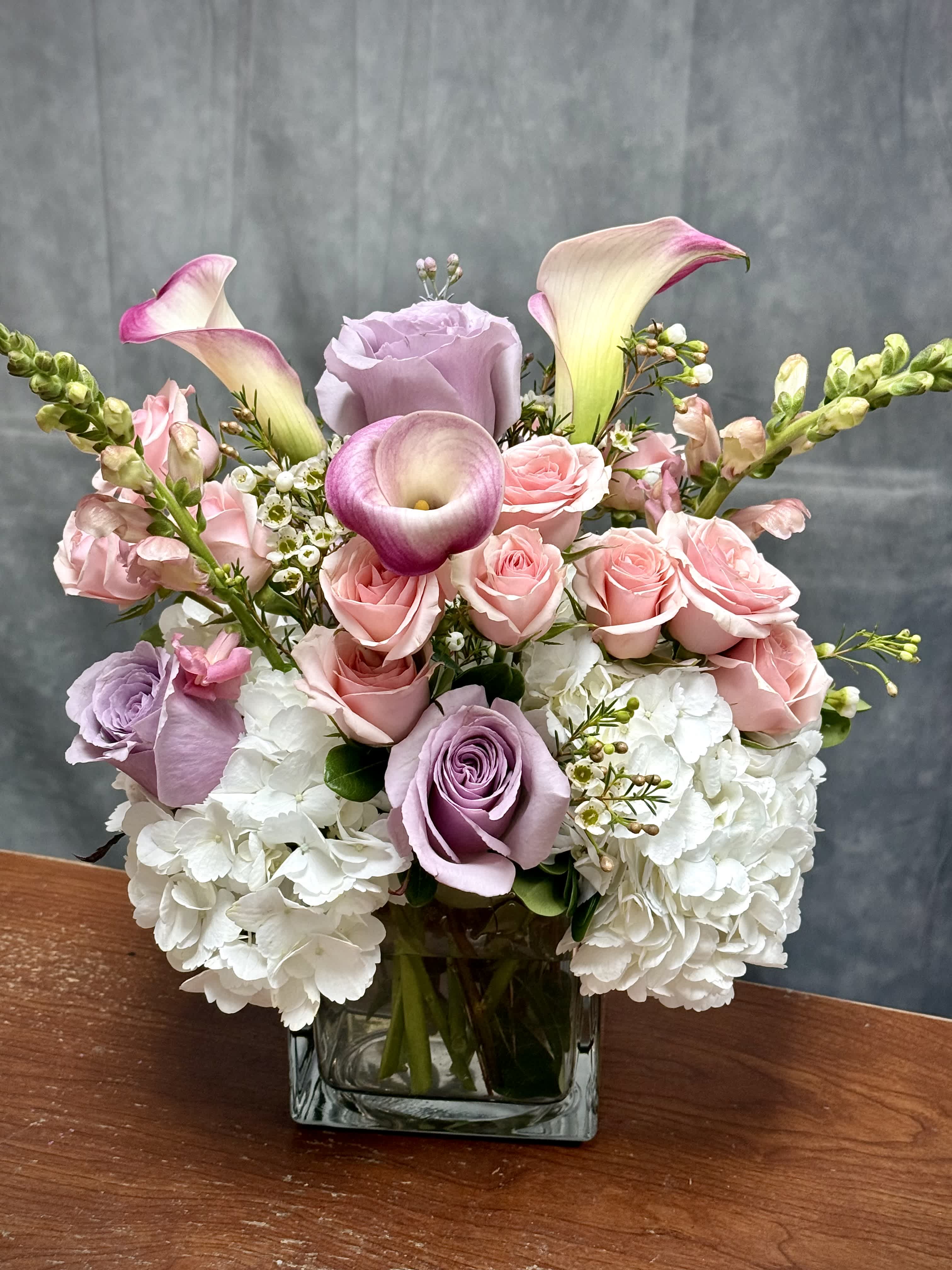 Pink roses and white hydrangeas in a square glass vase with calla lilies