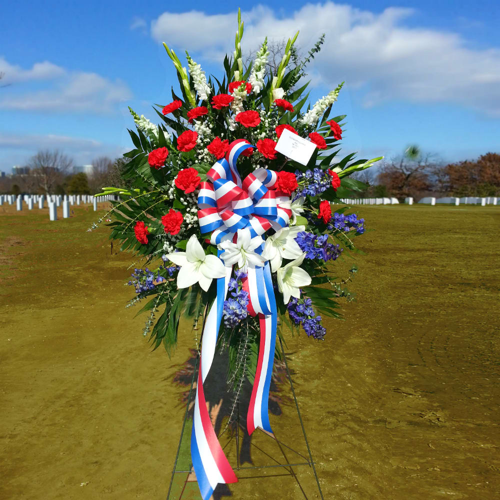 Standing funeral spray with red, white, and blue flowers and ribbon