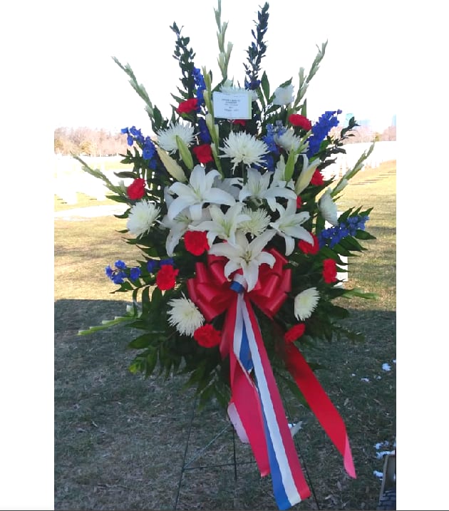 Large standing floral spray with white lilies, red carnations, and blue accents