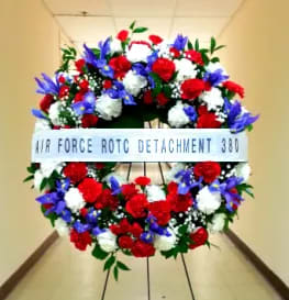 HOPE AND HONOR WREATH  WITH IRISES AND BANNER [TT-ANC47] - HOPE AND HONOR WREATH WITH IRISES AND HORIZONTAL BANNER BY TWIN TOWERS FLORIST.  A FRESH, PATRIOTIC FLORAL WREATH OF RED AND WHITE CARNATIONS, MINI CARNATIONS, BLUE IRISES, PREMIUM FILLERS AND GREENERY.  A SINGLE WHITE HORIZONTAL BANNER WITH BLACK TEXT IS INCLUDED.  STANDARD (AS SHOWN): 24" DIAMETER DELUXE:  30" DIAMETER PREMIUM: 36" DIAMETER