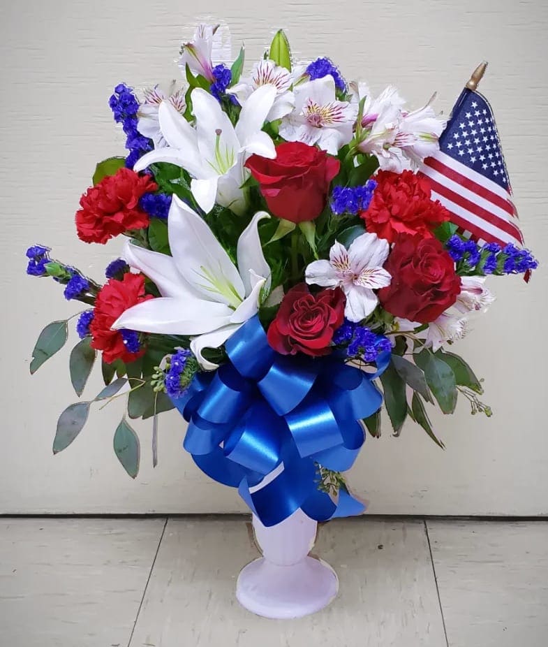 Red roses and white lilies in a vase with a blue ribbon and small American flag